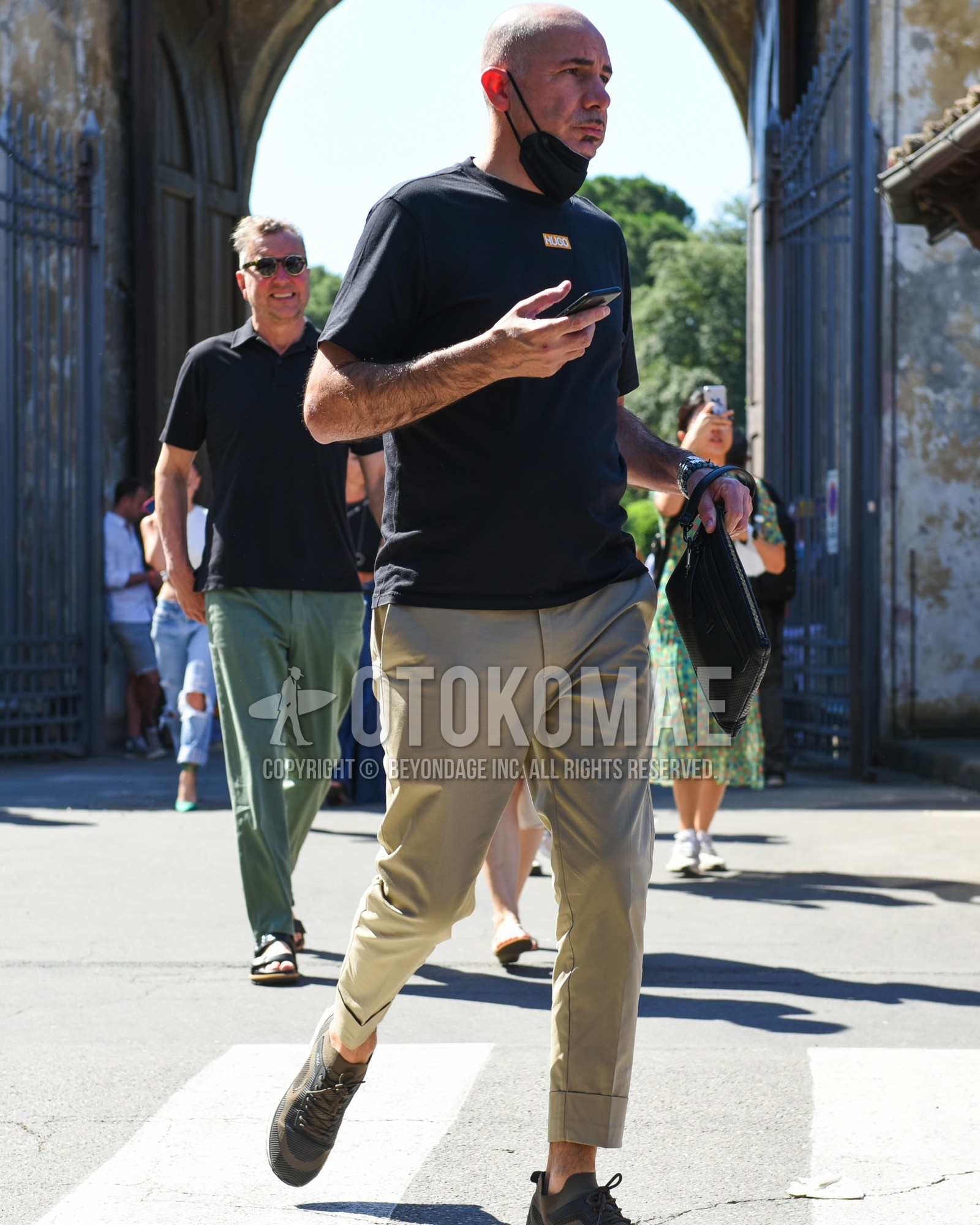Men's spring summer outfit with black one point t-shirt, beige plain chinos, olive green low-cut sneakers.