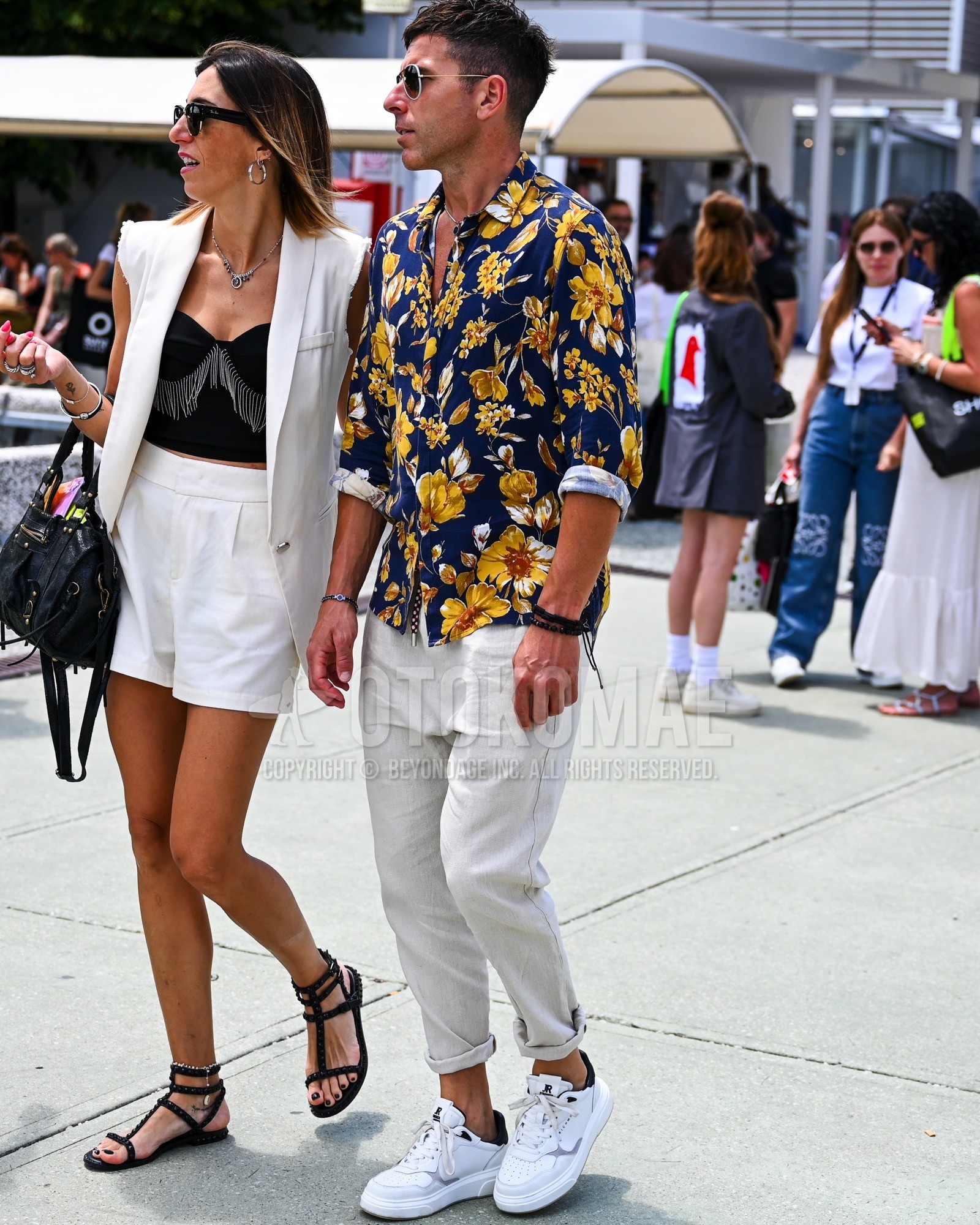 Men's spring summer autumn outfit with black plain sunglasses, navy whole pattern shirt, white plain chinos, white low-cut sneakers.