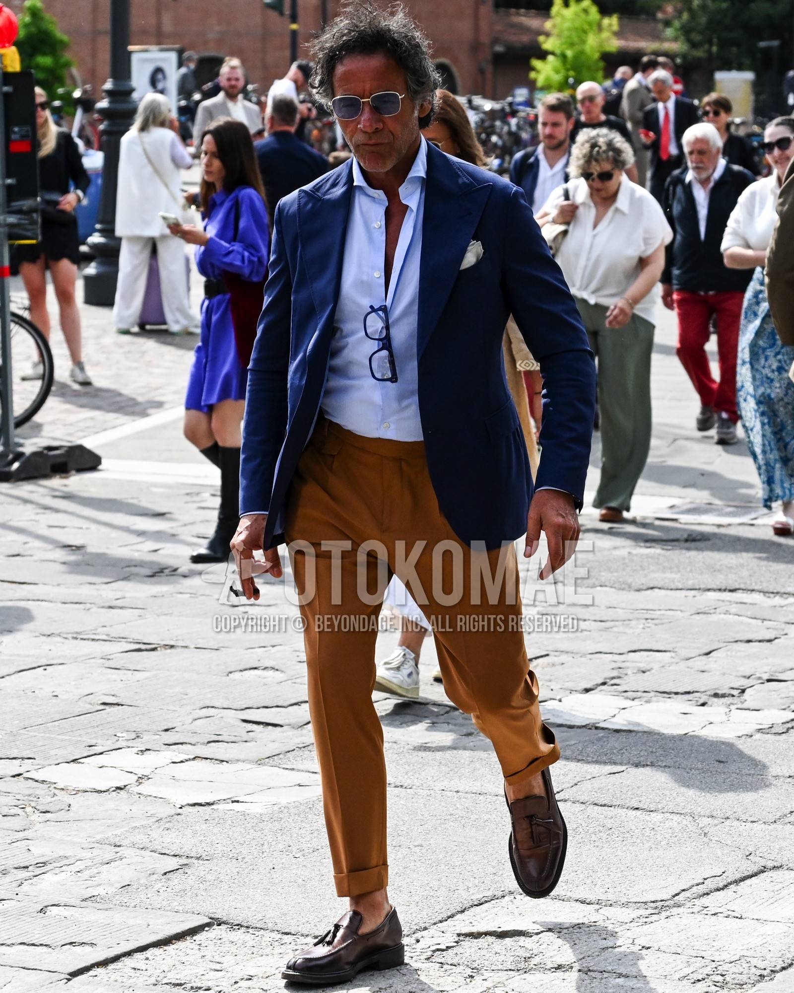 Men's spring summer autumn outfit with blue plain sunglasses, navy plain tailored jacket, light blue plain shirt, brown plain chinos, brown tassel loafers leather shoes.