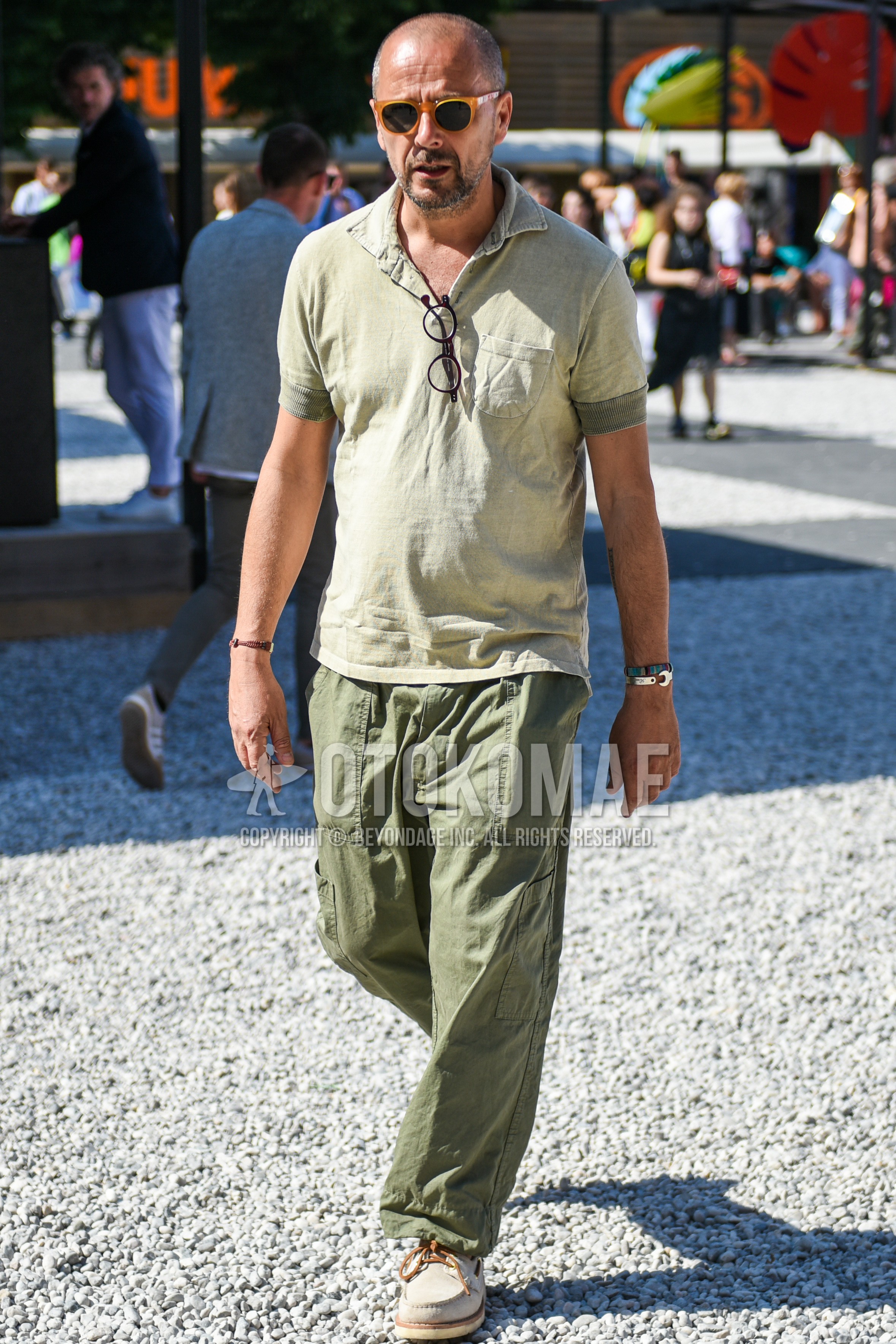 Men's summer outfit with beige plain sunglasses, green plain polo shirt, olive green plain chinos.