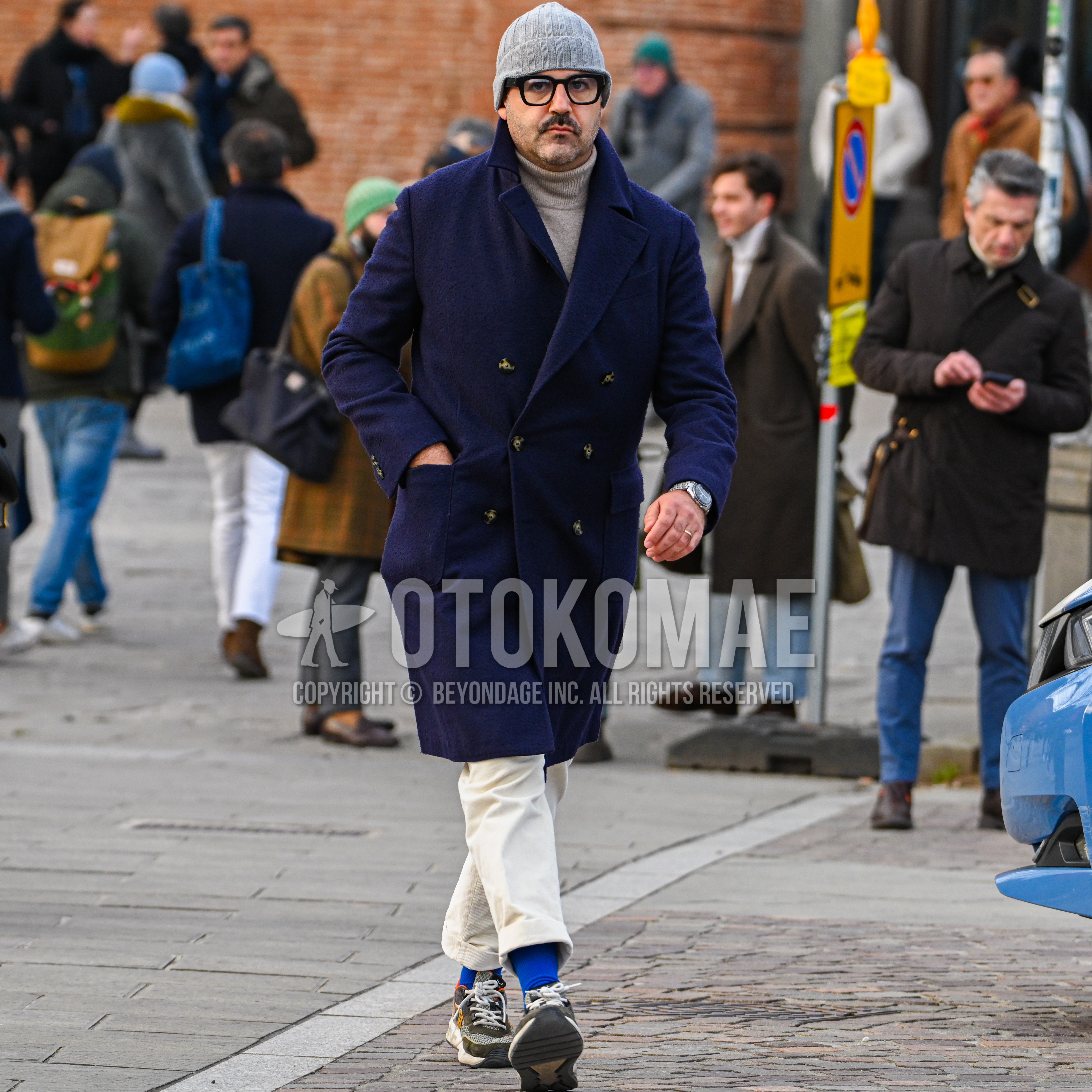 Men's autumn winter outfit with gray plain knit cap, black plain glasses, navy plain p coat, beige plain turtleneck knit, white plain cotton pants, blue plain socks, multi-color low-cut sneakers.