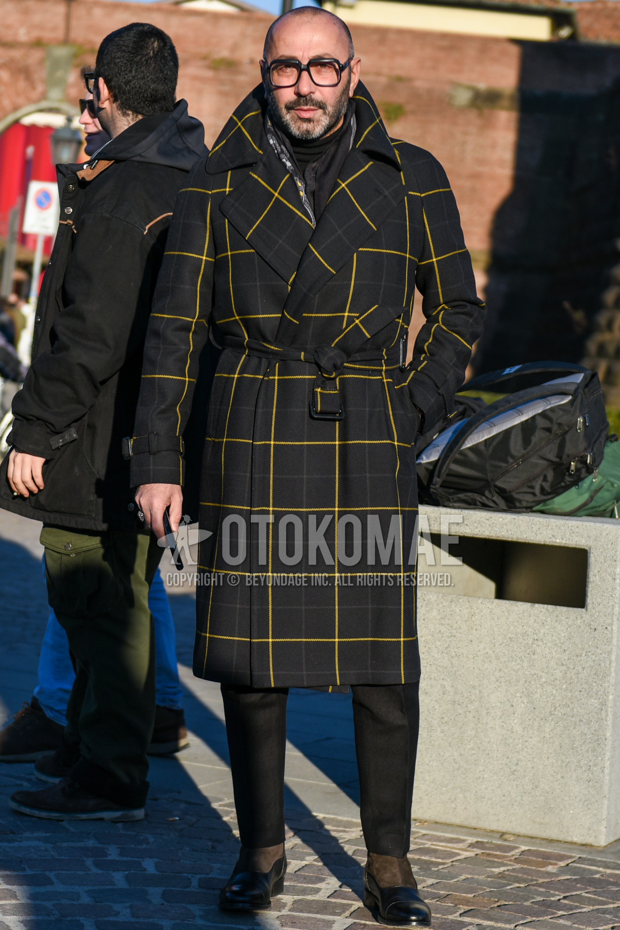 Men's autumn winter outfit with black plain glasses, black yellow plain belted coat, black plain turtleneck knit, dark gray plain slacks, dark gray plain cropped pants, black brown  boots.