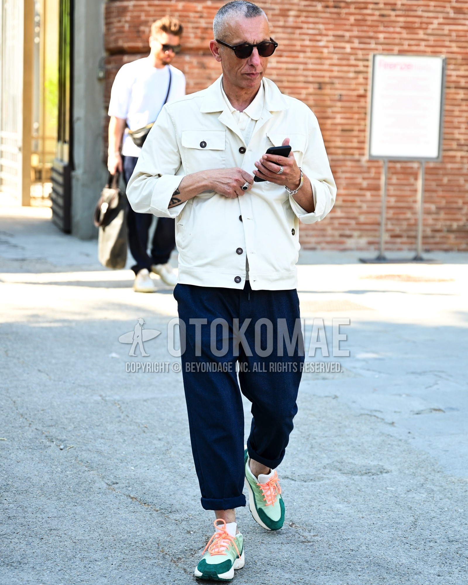 Men's spring summer autumn outfit with black plain sunglasses, white plain tailored jacket, white plain shirt, navy plain chinos, green low-cut sneakers.