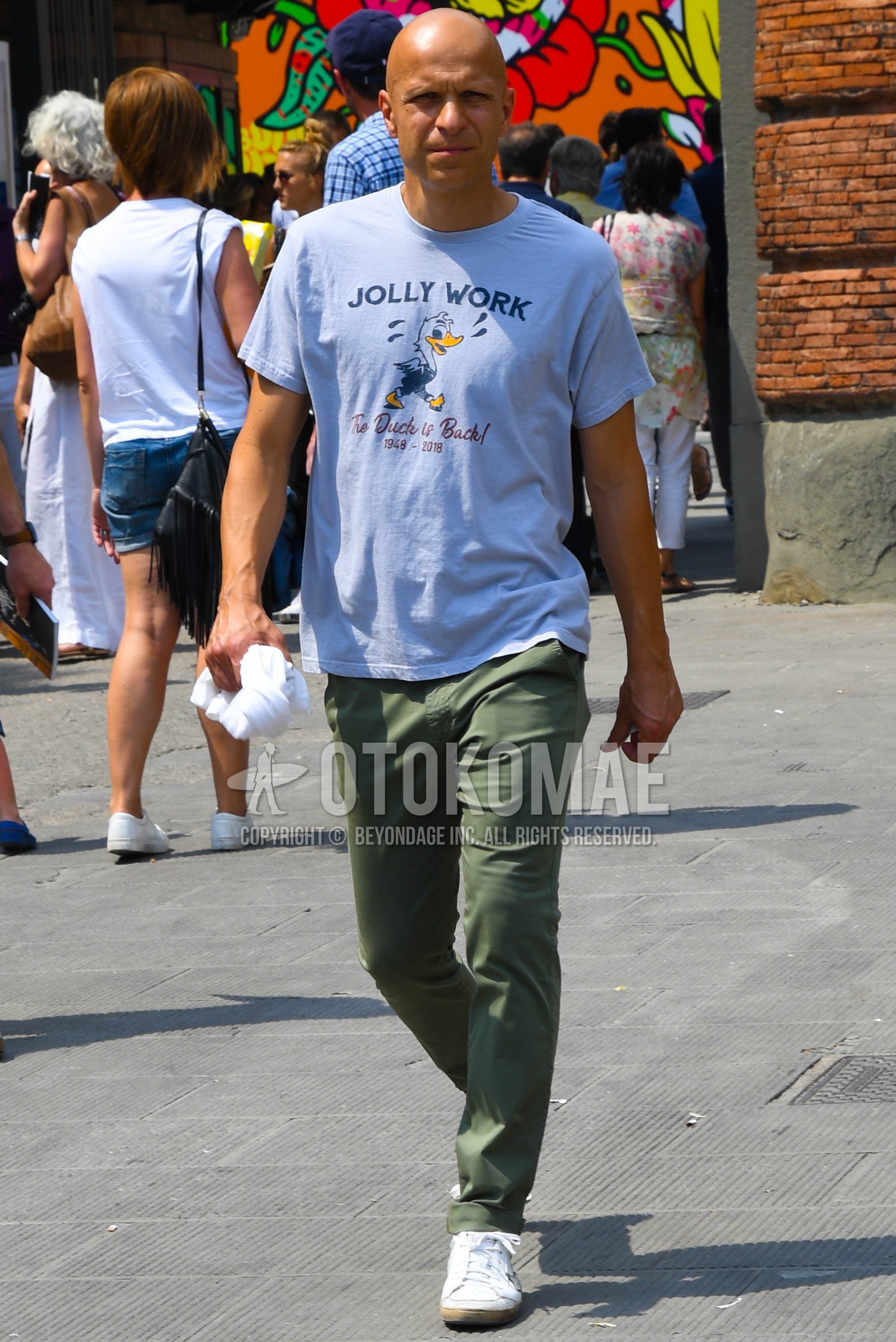 Men's spring summer outfit with gray graphic t-shirt, olive green plain chinos, white low-cut sneakers.