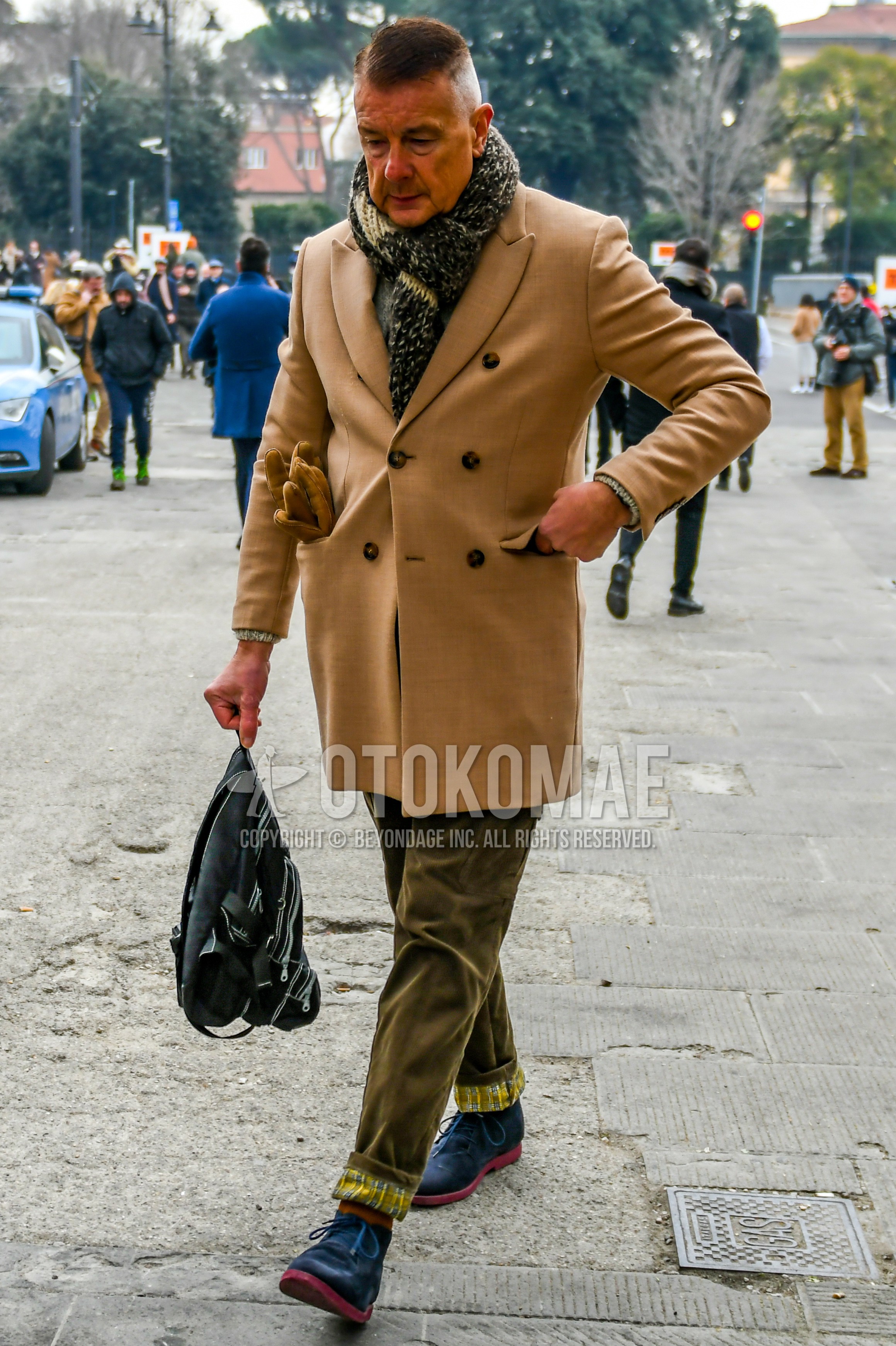 Men's winter outfit with black plain scarf, beige plain chester coat, olive green plain winter pants (corduroy,velour), brown plain socks, navy chukka boots, black plain backpack.