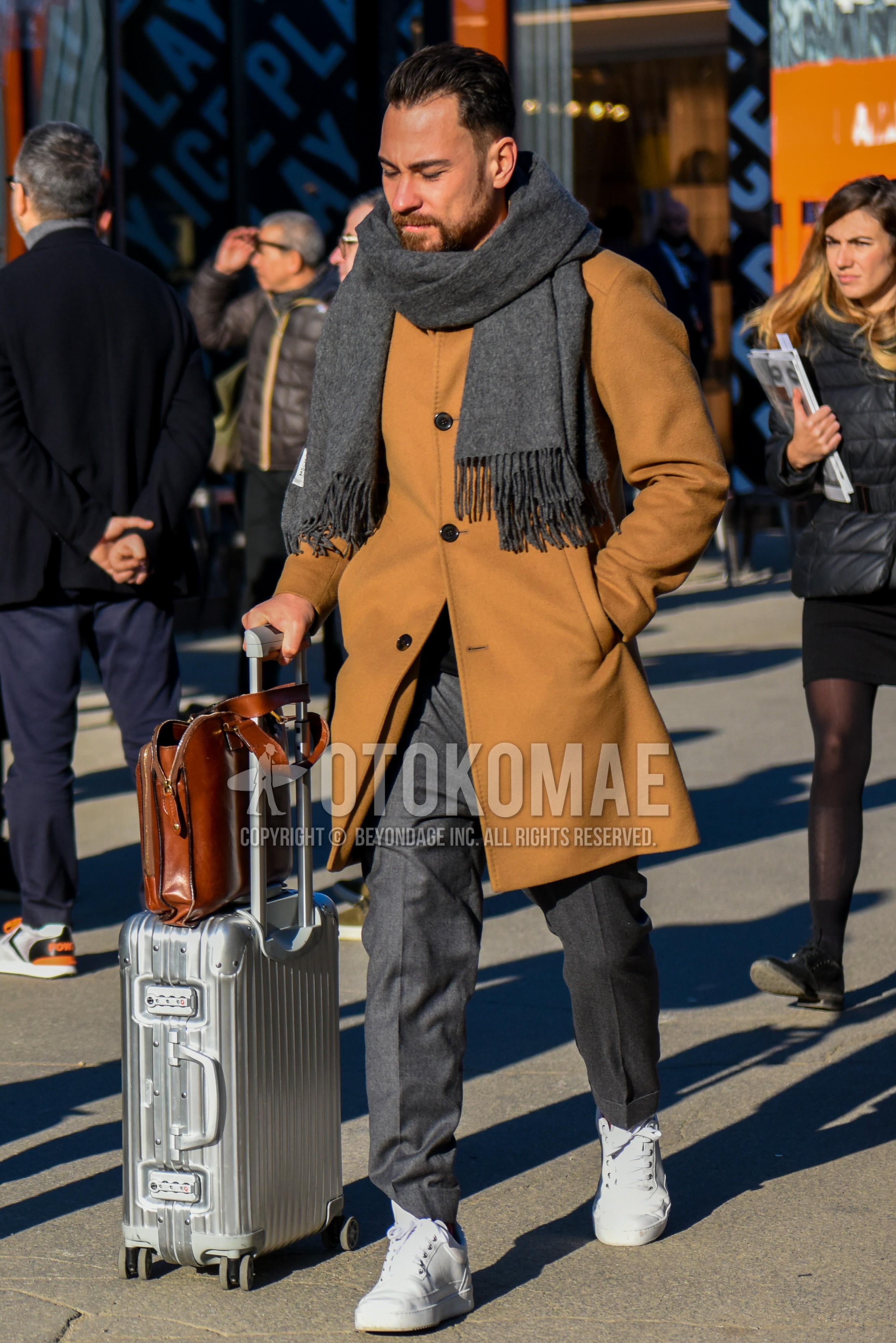 Men's winter outfit with dark gray plain scarf, brown plain chester coat, dark gray plain slacks, white high-cut sneakers, brown plain shoulder bag.