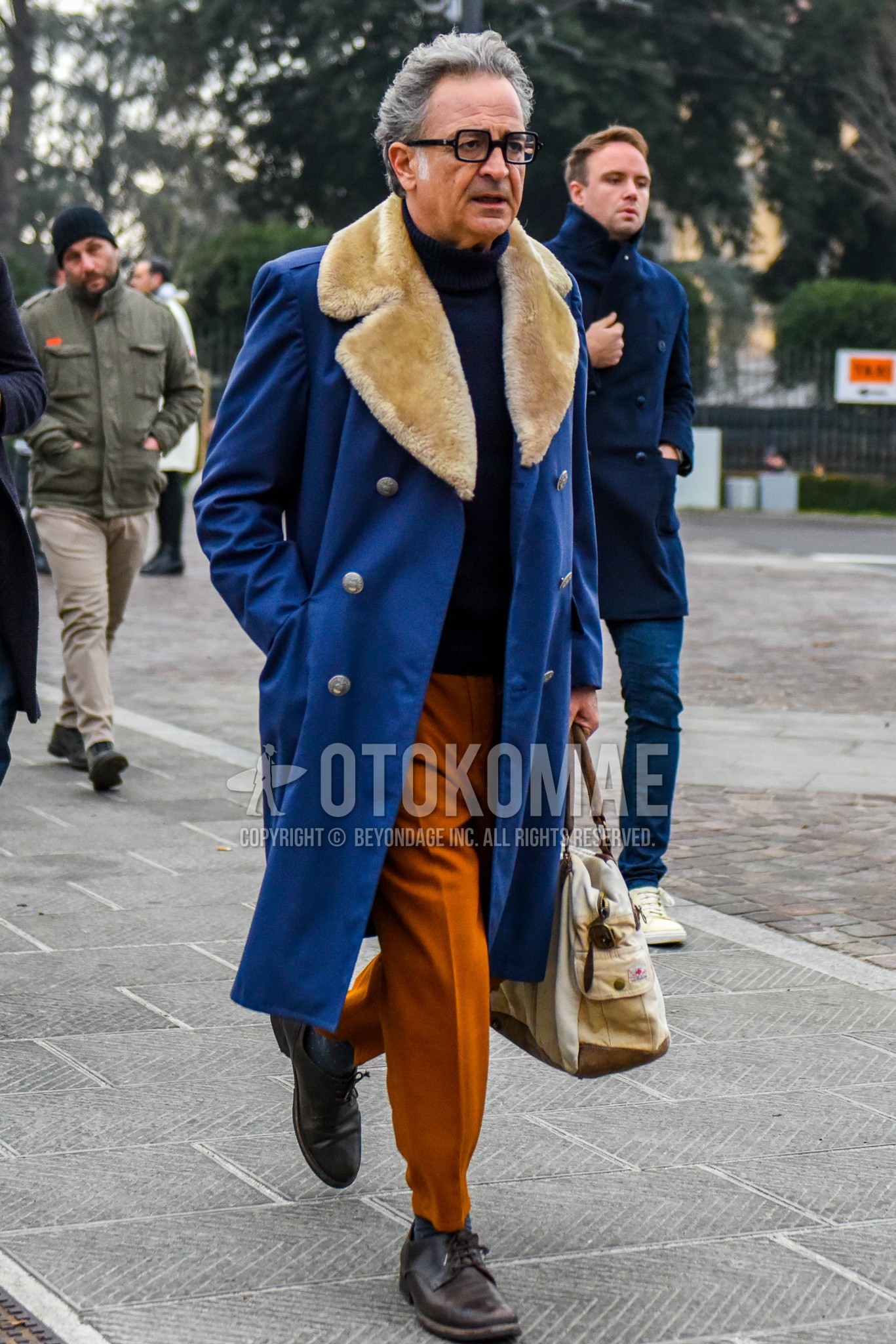 Men's winter outfit with black plain glasses, blue plain ulster coat, navy plain turtleneck knit, orange plain slacks, brown plain toe leather shoes, white plain boston bag.