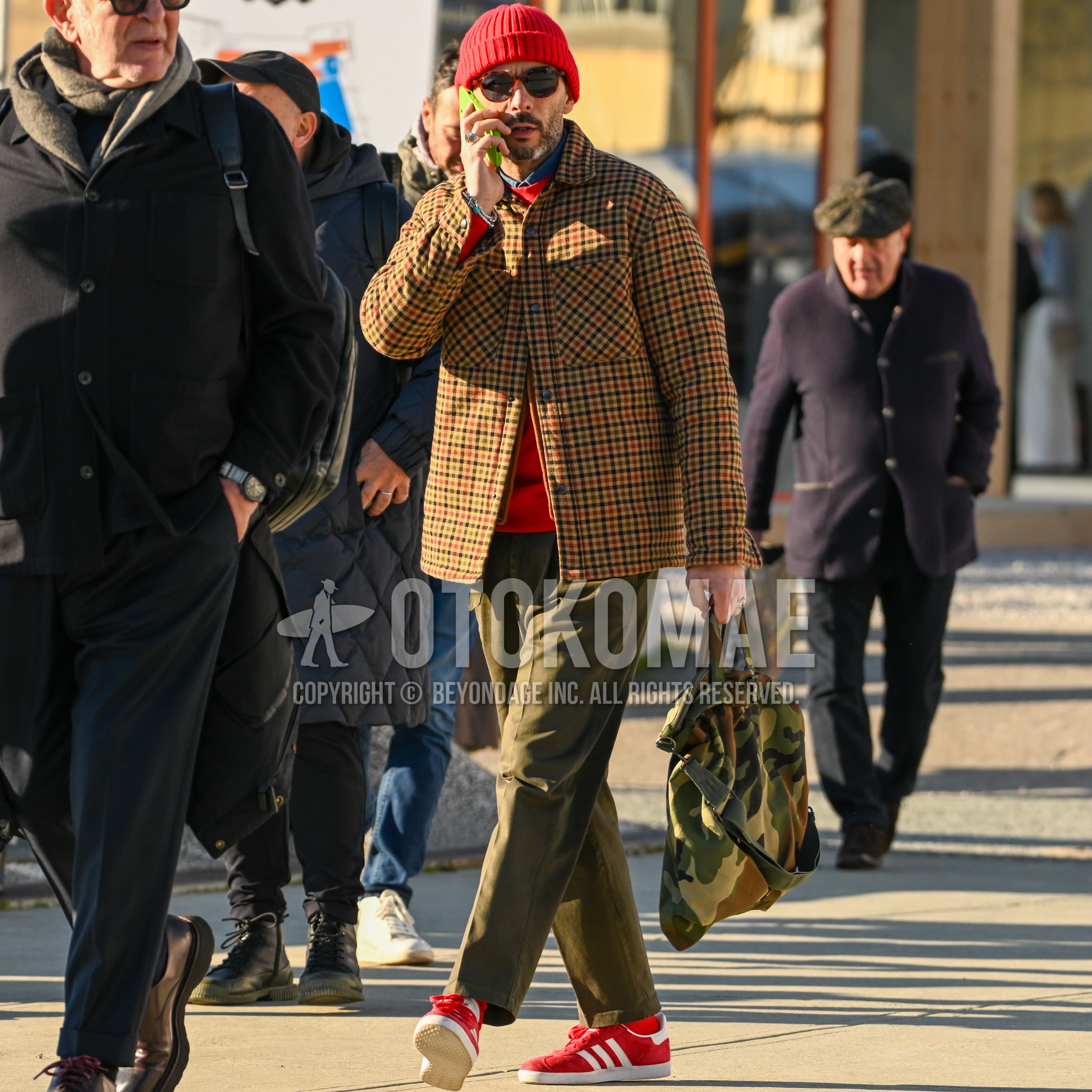 Men's autumn winter outfit with red plain knit cap, tortoiseshell sunglasses, brown check coverall, plain denim shirt/chambray shirt, red plain sweatshirt, olive green plain chinos, red plain socks, red low-cut sneakers, camouflage briefcase/handbag.