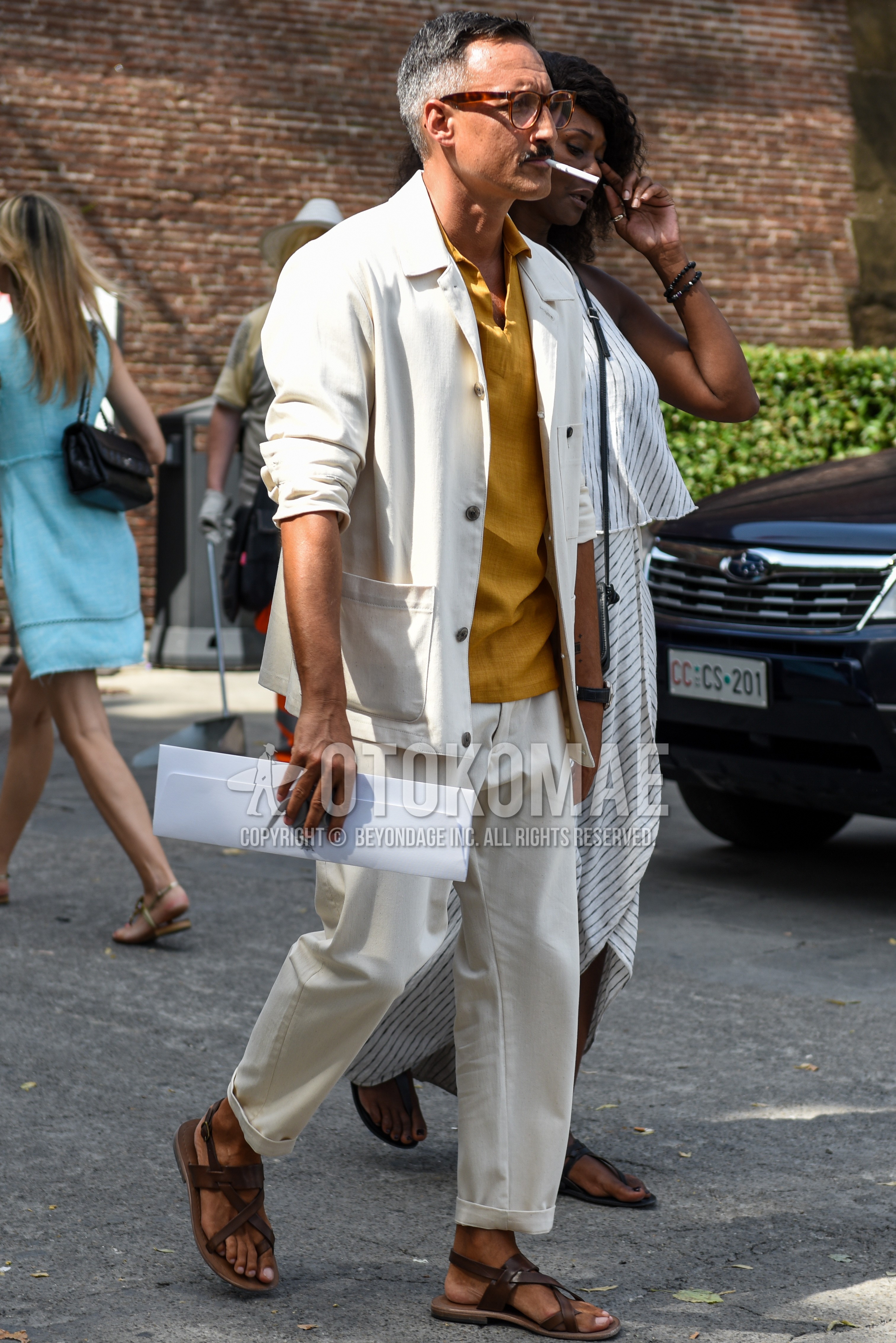 Men's spring summer outfit with brown tortoiseshell glasses, white plain shirt jacket, yellow plain shirt, white plain cotton pants, brown leather sandals.