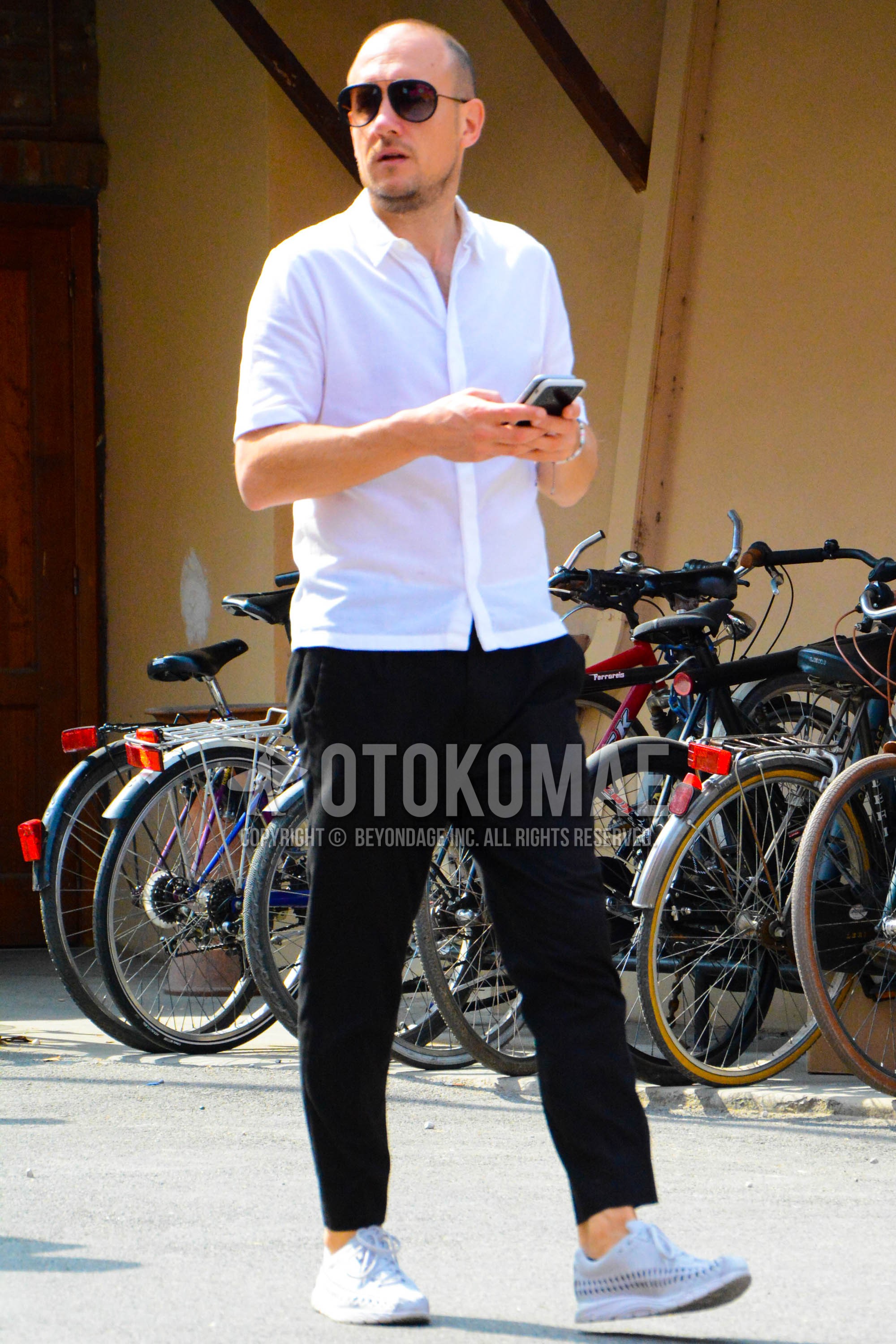 Men's spring summer outfit with black plain sunglasses, white plain shirt, black plain chinos, white low-cut sneakers.