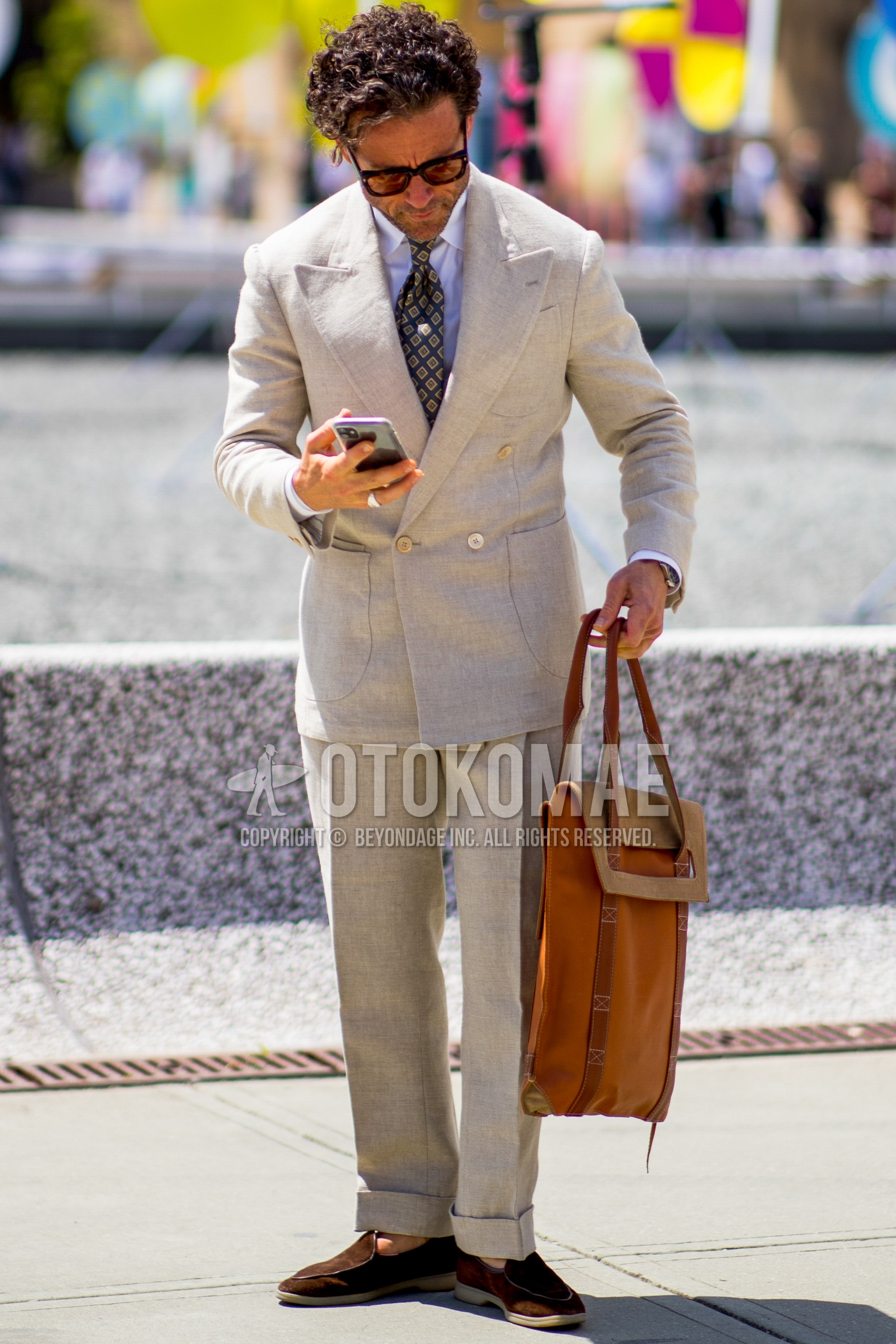 Men's spring outfit with black plain sunglasses, white plain shirt, brown suede shoes leather shoes, brown plain tote bag, gray plain suit, navy small crest necktie.