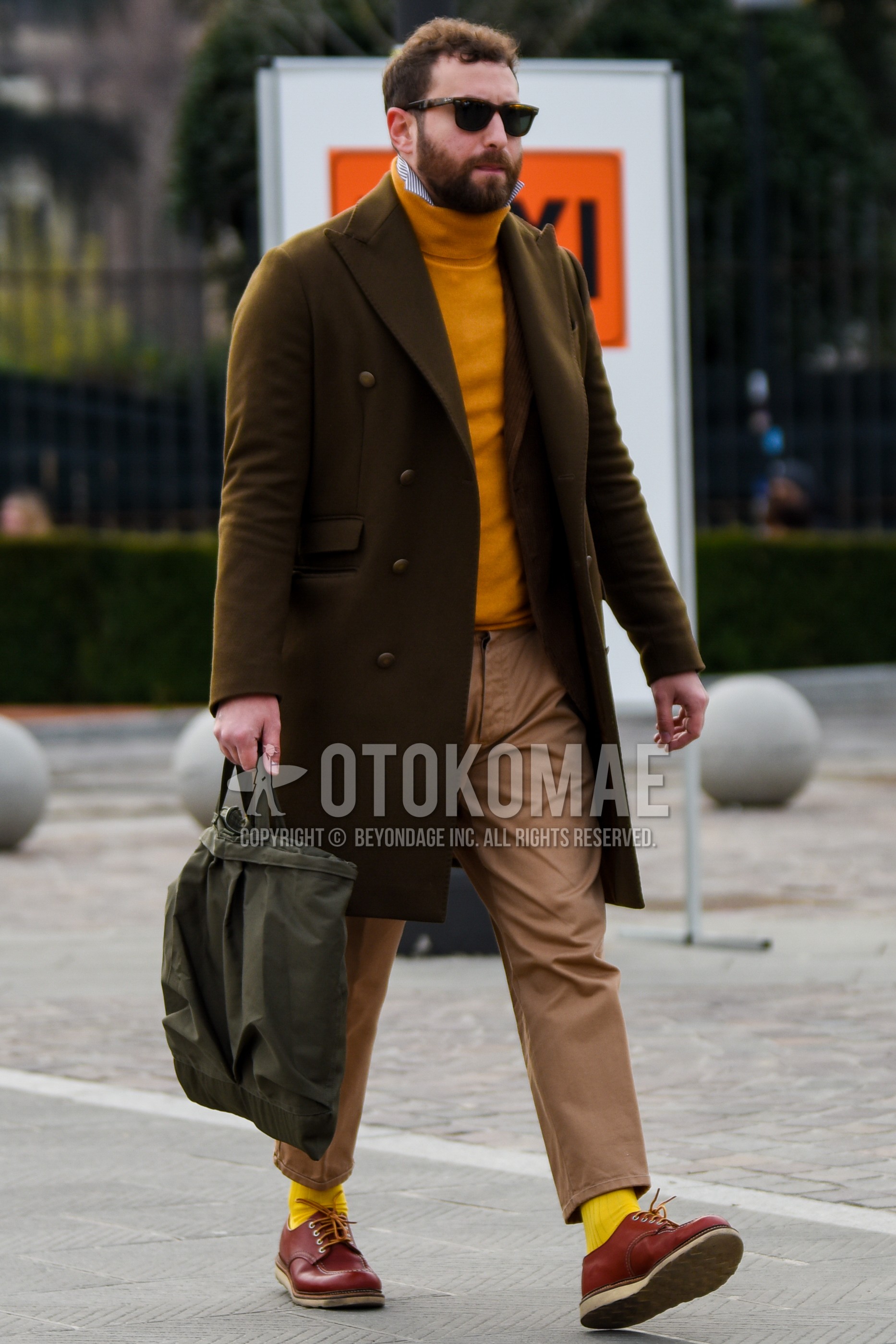Men's autumn winter outfit with brown tortoiseshell sunglasses, olive green plain chester coat, yellow plain turtleneck knit, beige plain chinos, beige plain ankle pants, yellow plain socks, brown  leather shoes, olive green plain briefcase/handbag.