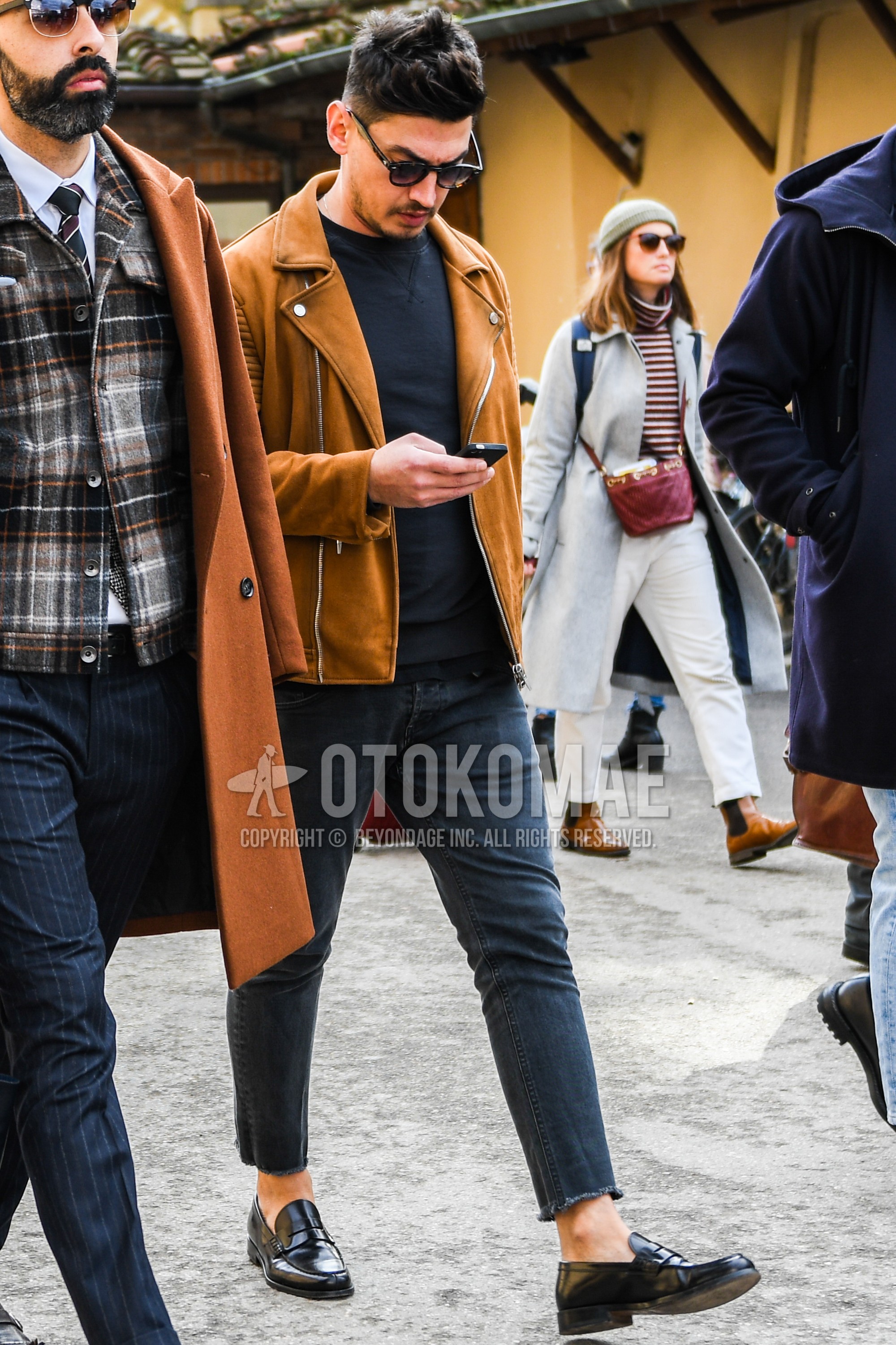 Men's spring autumn outfit with plain sunglasses, brown plain riders jacket, black plain sweatshirt, black plain denim/jeans, black coin loafers leather shoes.