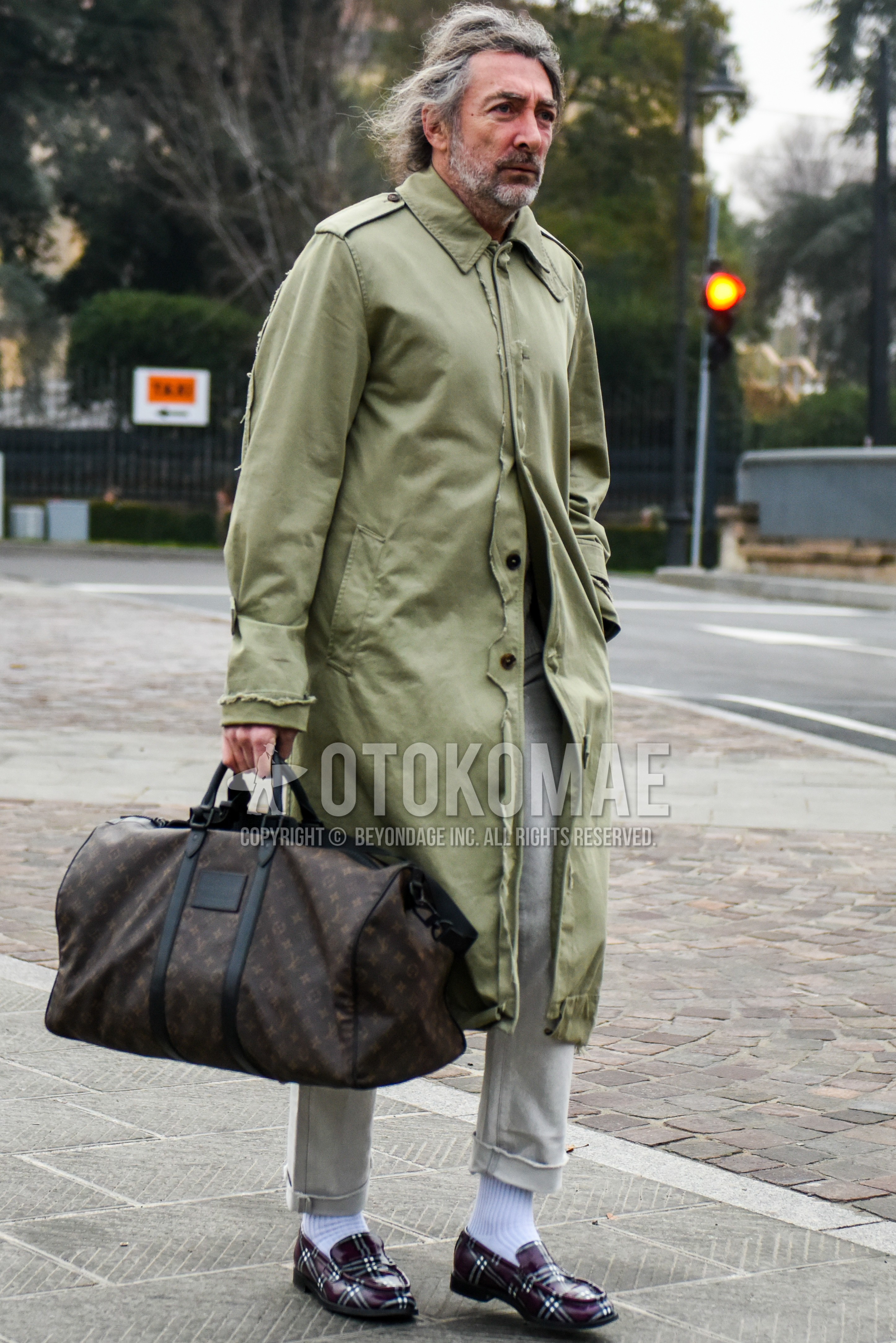 Men's autumn winter outfit with olive green plain stenkarrer coat, beige plain cotton pants, white plain socks, brown coin loafers leather shoes, brown bag boston bag.