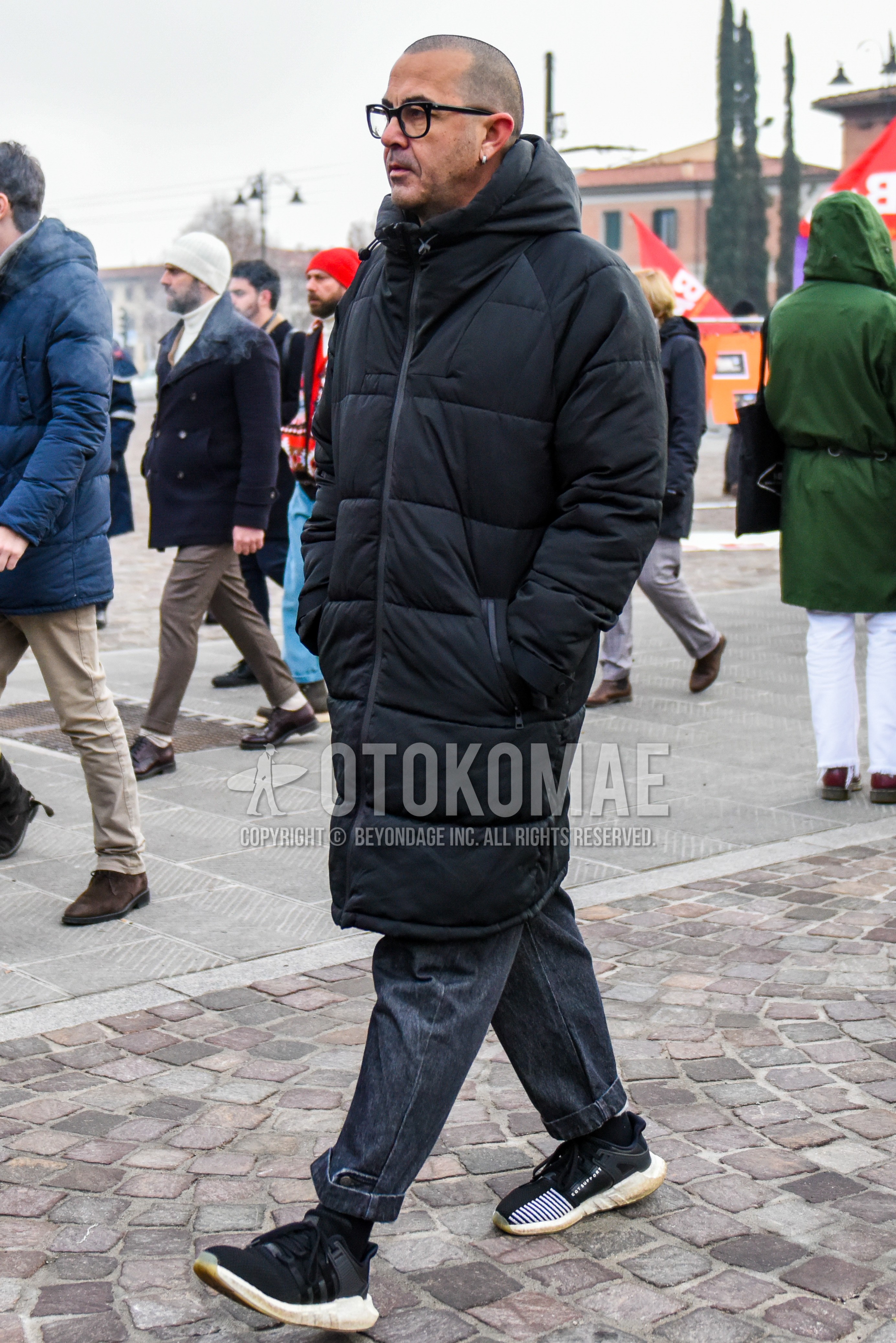 Men's winter outfit with plain glasses, black plain down jacket, gray plain denim/jeans, black plain socks, black low-cut sneakers.