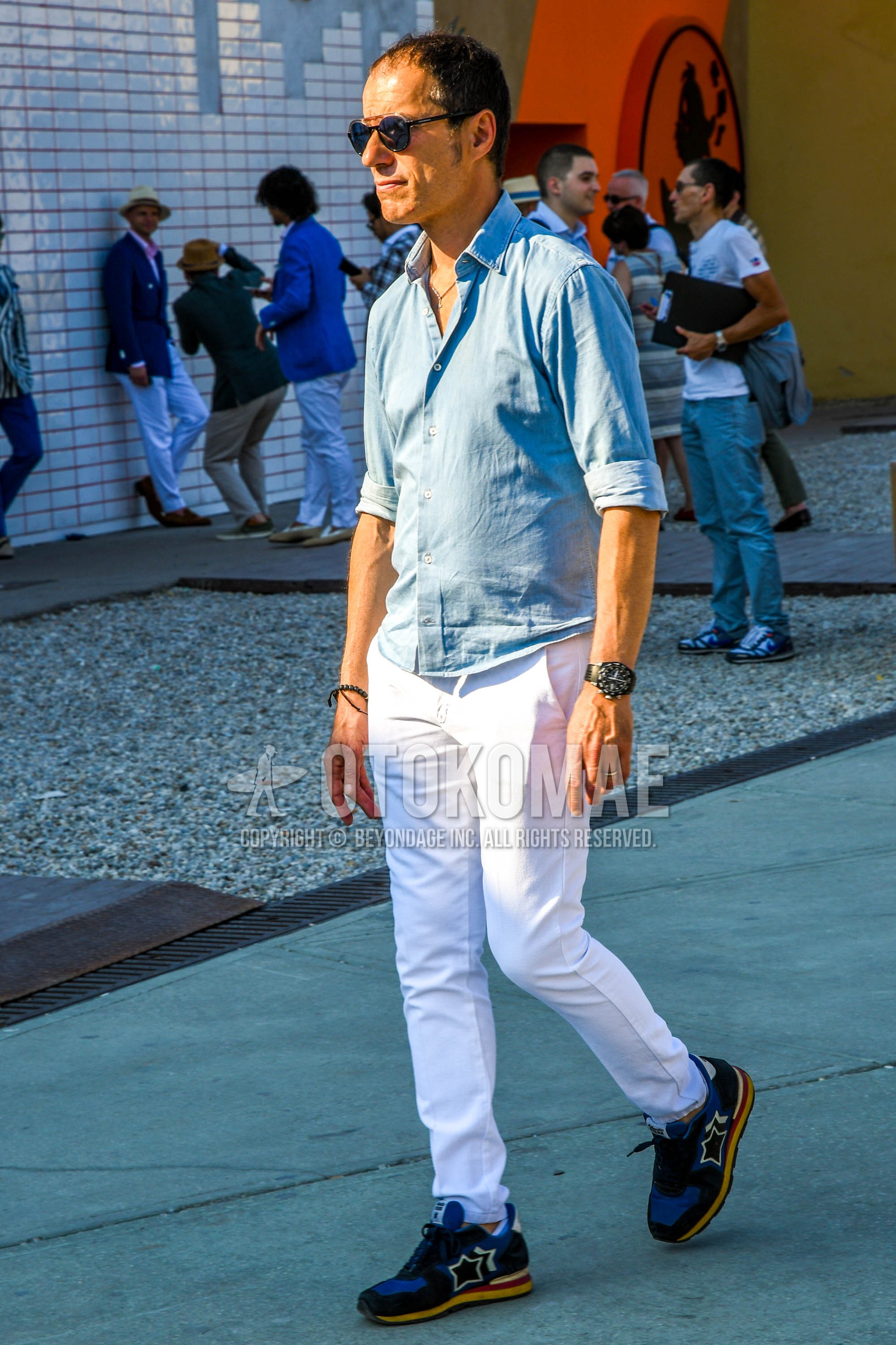 Men's spring summer autumn outfit with plain sunglasses, light blue plain shirt, white plain chinos, blue low-cut sneakers.