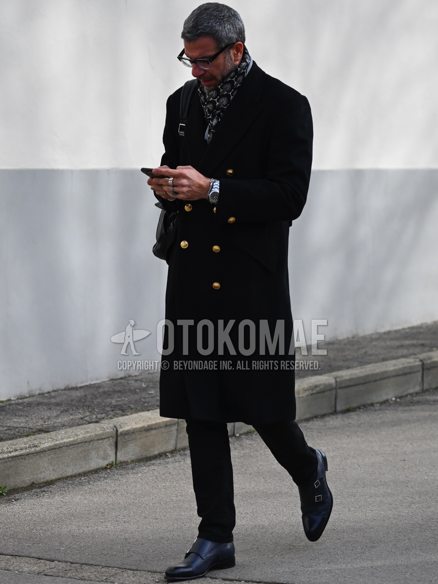 Men's autumn winter outfit with black plain glasses, gray graphic scarf, black plain chester coat, black plain slacks, black monk shoes leather shoes, black plain shoulder bag.