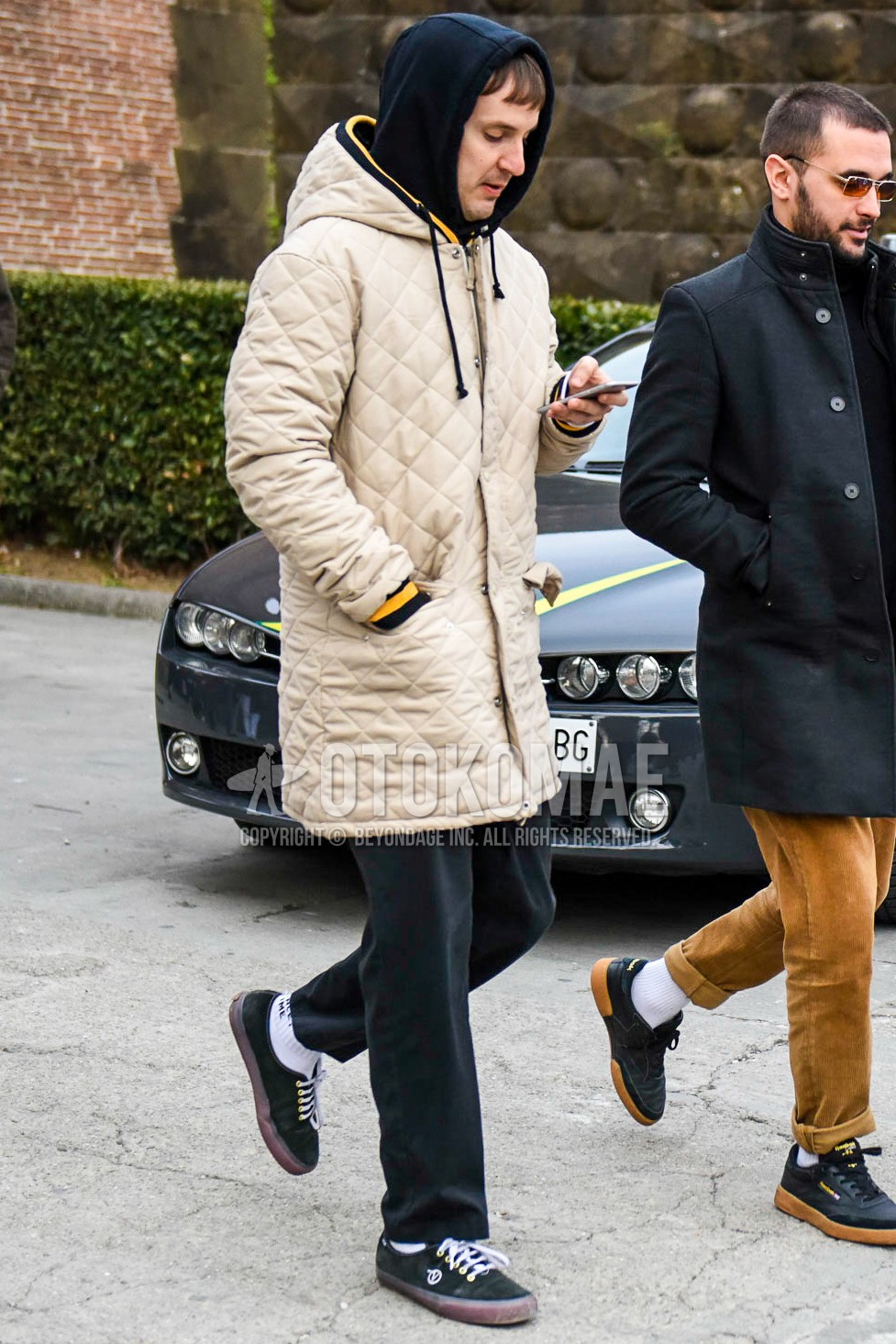 Men's winter outfit with beige plain quilted jacket, black plain hoodie, black plain cotton pants, white plain socks, black low-cut sneakers.