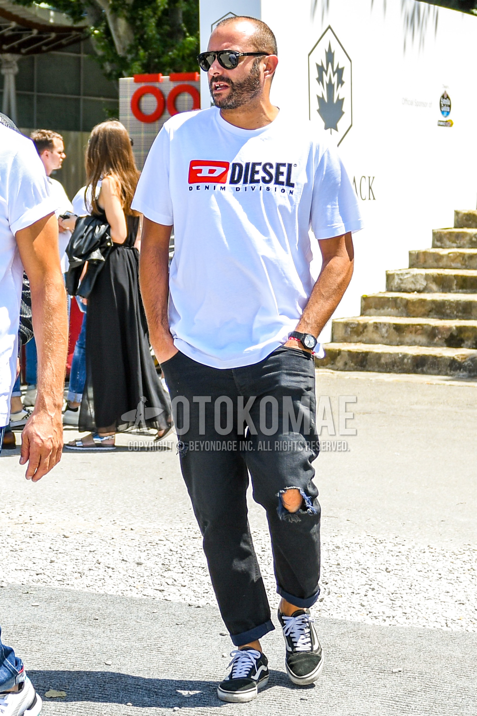 Men's summer outfit with plain sunglasses, white deca logo t-shirt, dark gray plain damaged jeans, black low-cut sneakers.