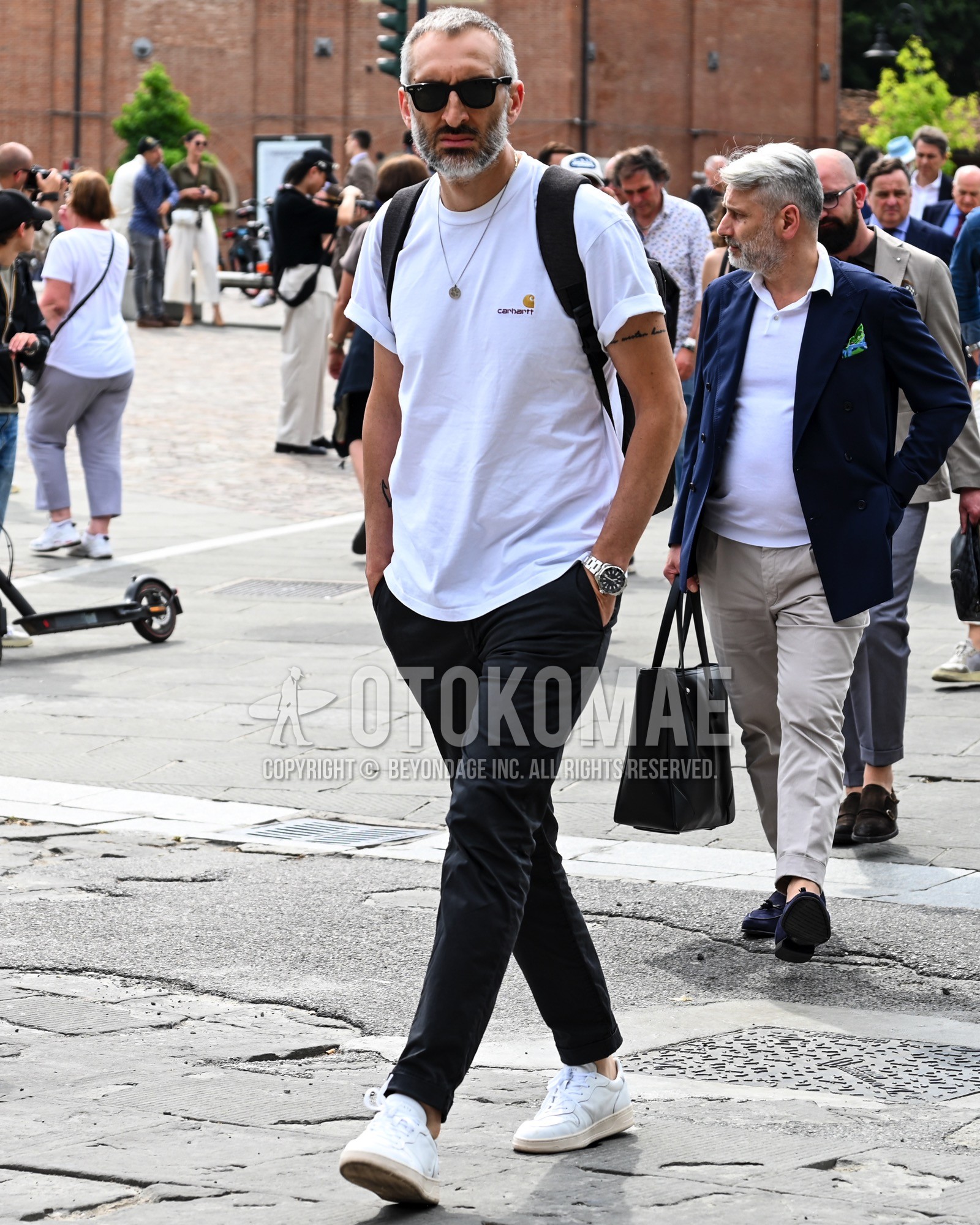Men's spring summer outfit with black plain sunglasses, white one point t-shirt, black plain chinos, white low-cut sneakers, black plain backpack.