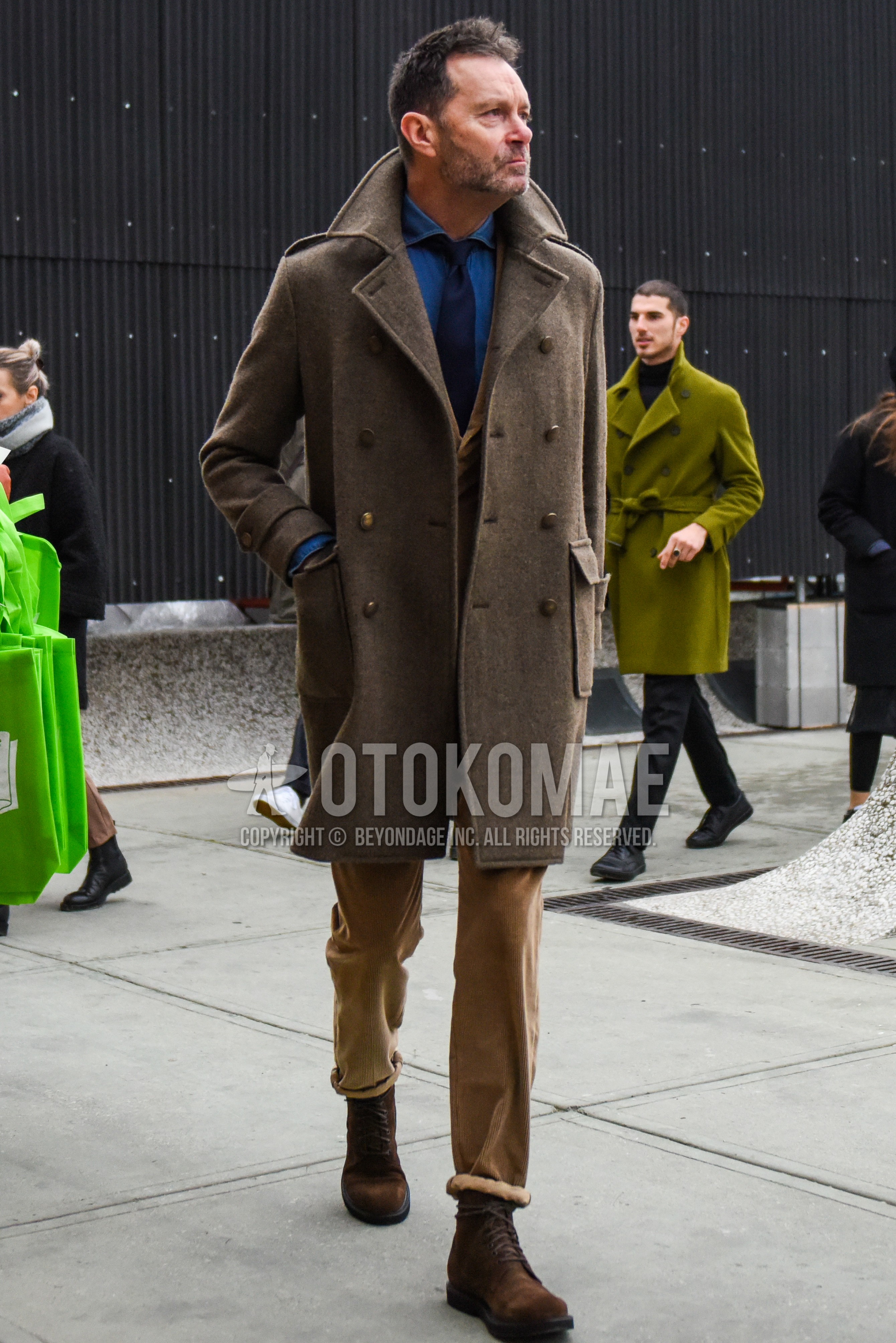 Men's winter outfit with beige plain ulster coat, beige plain tailored jacket, blue plain denim shirt/chambray shirt, beige plain winter pants (corduroy,velour), brown  boots, navy plain necktie.