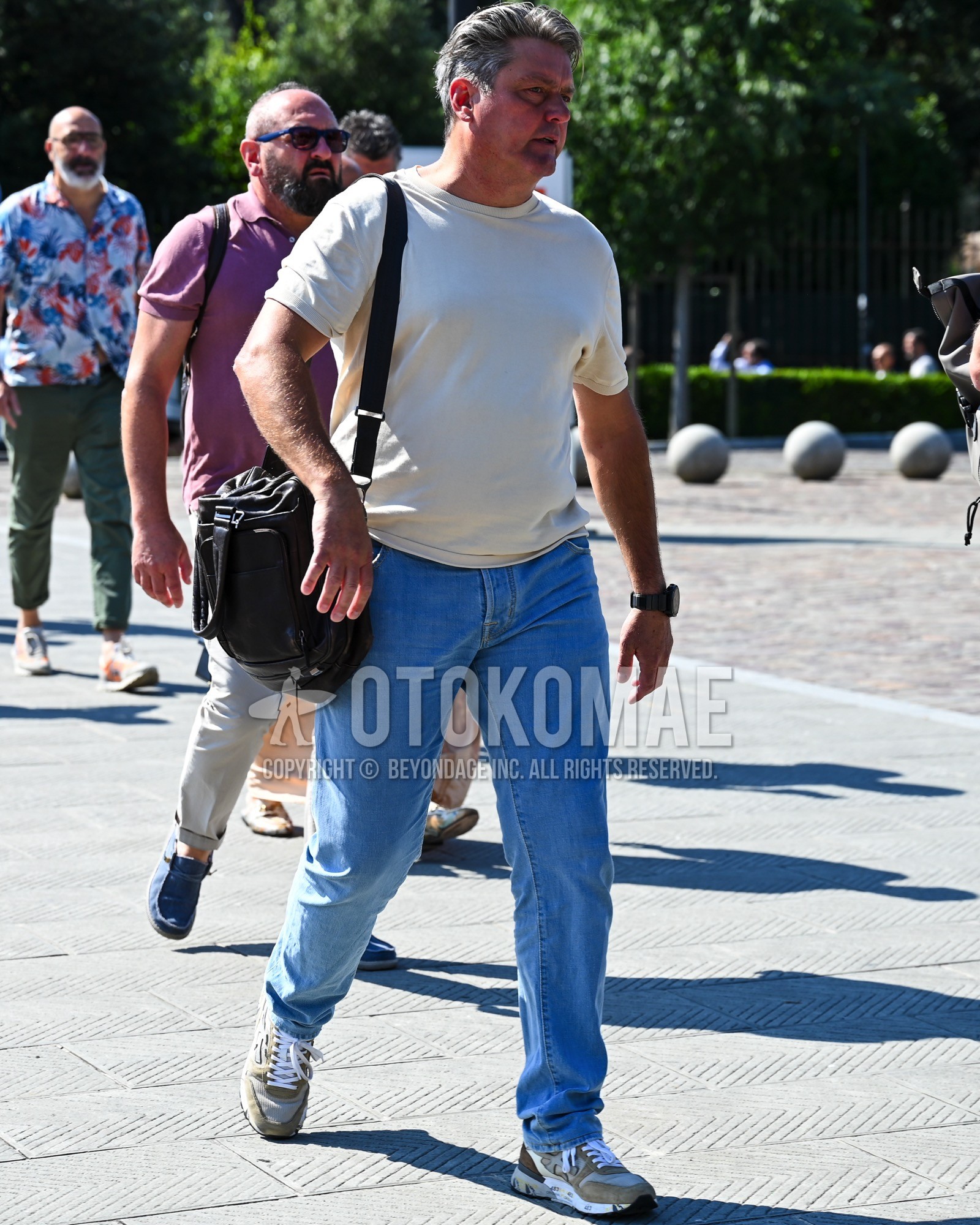 Men's spring summer outfit with white plain t-shirt, blue plain denim/jeans, beige low-cut sneakers, black plain shoulder bag.