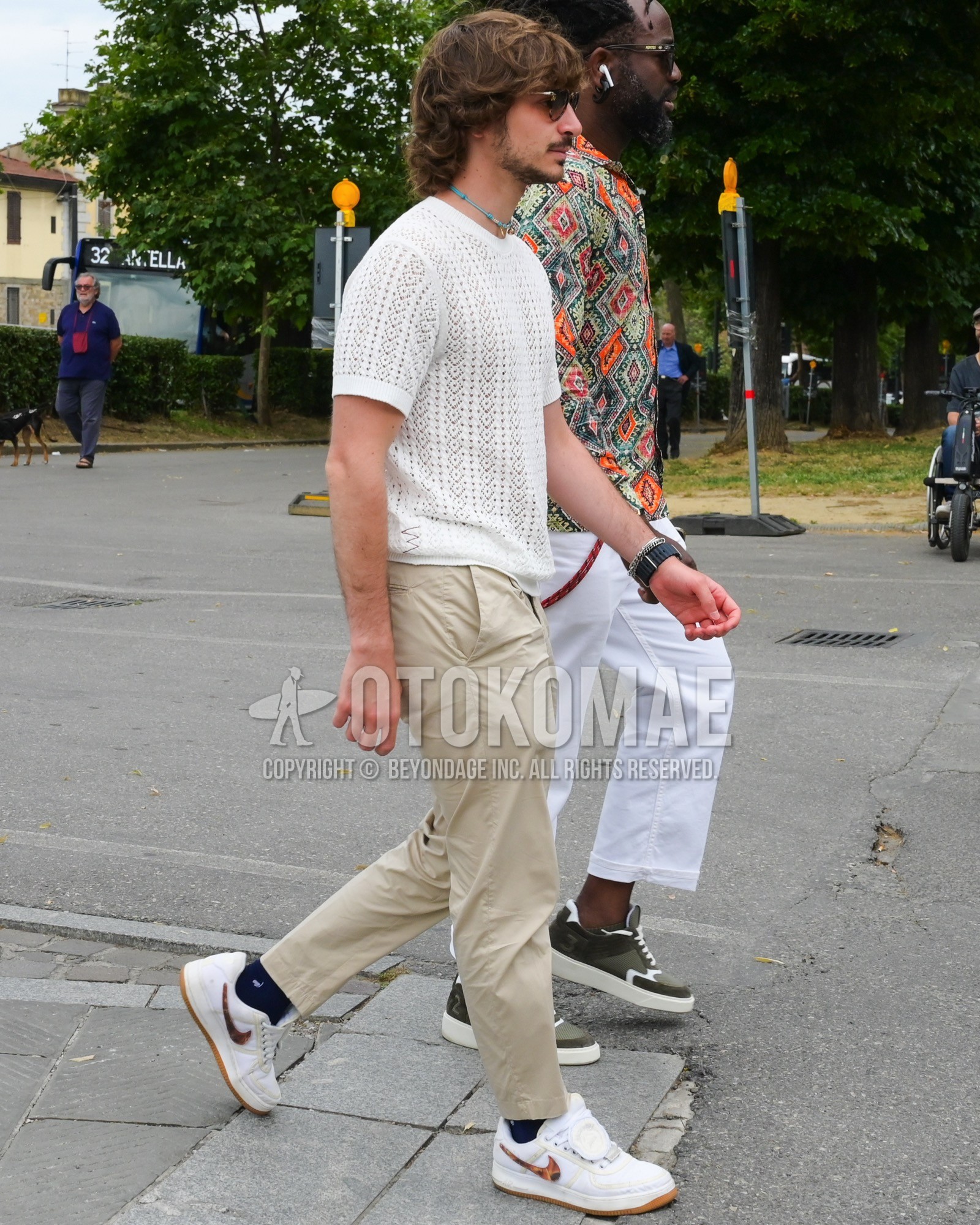 Men's spring summer outfit with white plain t-shirt, beige plain chinos, black plain socks, white low-cut sneakers.