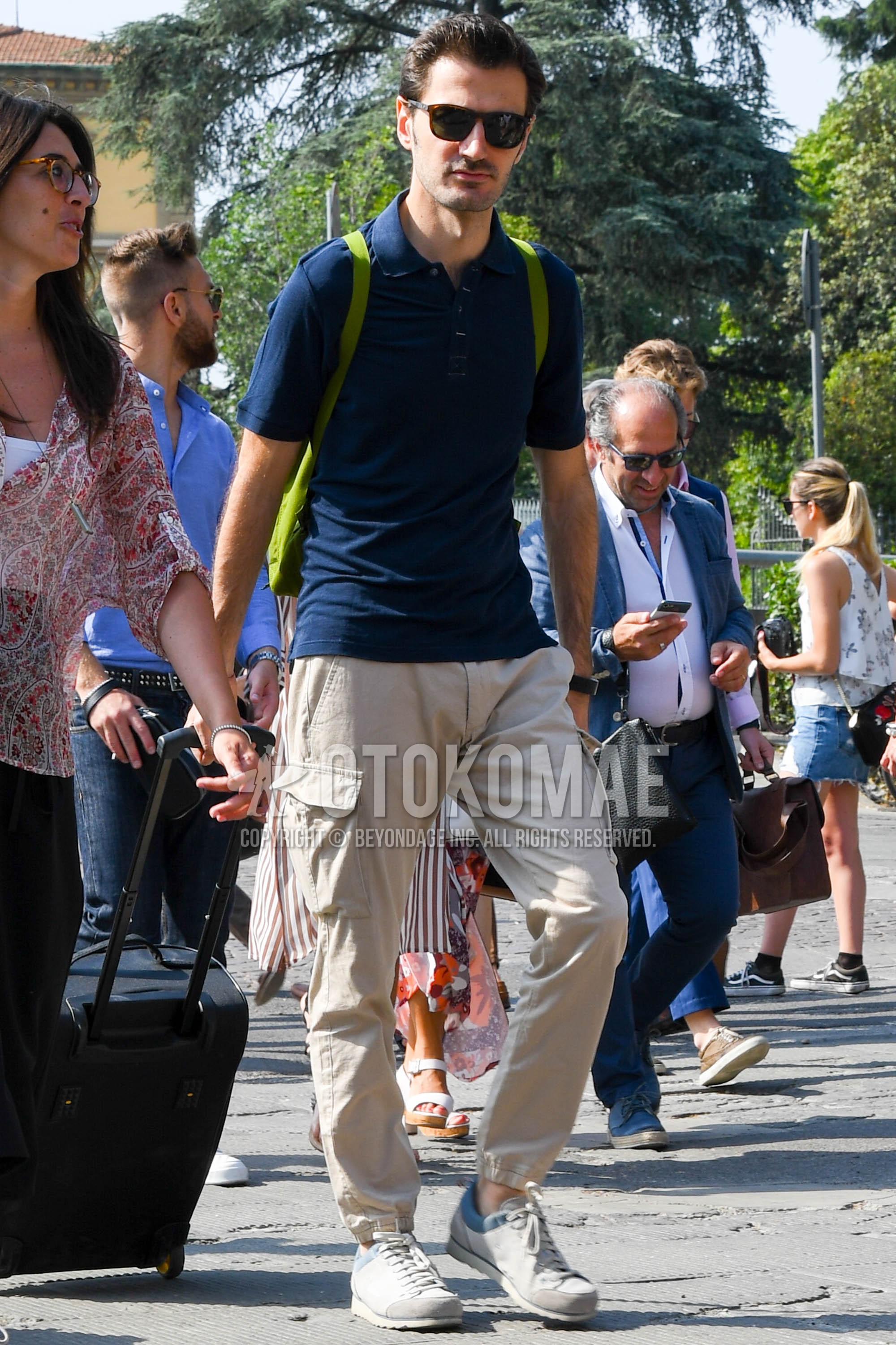 Men's summer outfit with tortoiseshell sunglasses, navy plain polo shirt, beige plain cargo pants, gray low-cut sneakers.