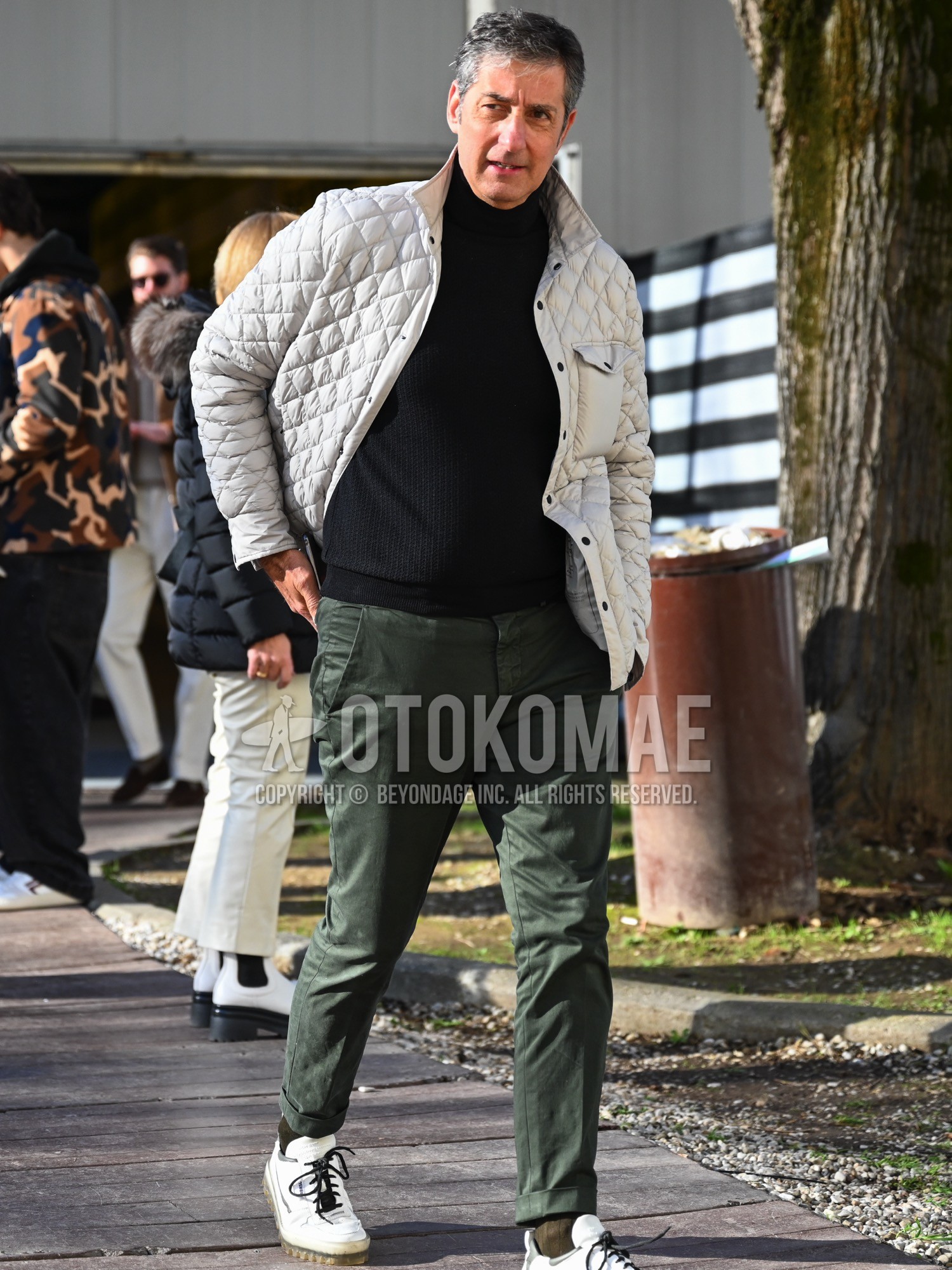Men's spring autumn winter outfit with white plain quilted jacket, black plain turtleneck knit, green plain ankle pants, green plain chinos, olive green plain socks, white low-cut sneakers.