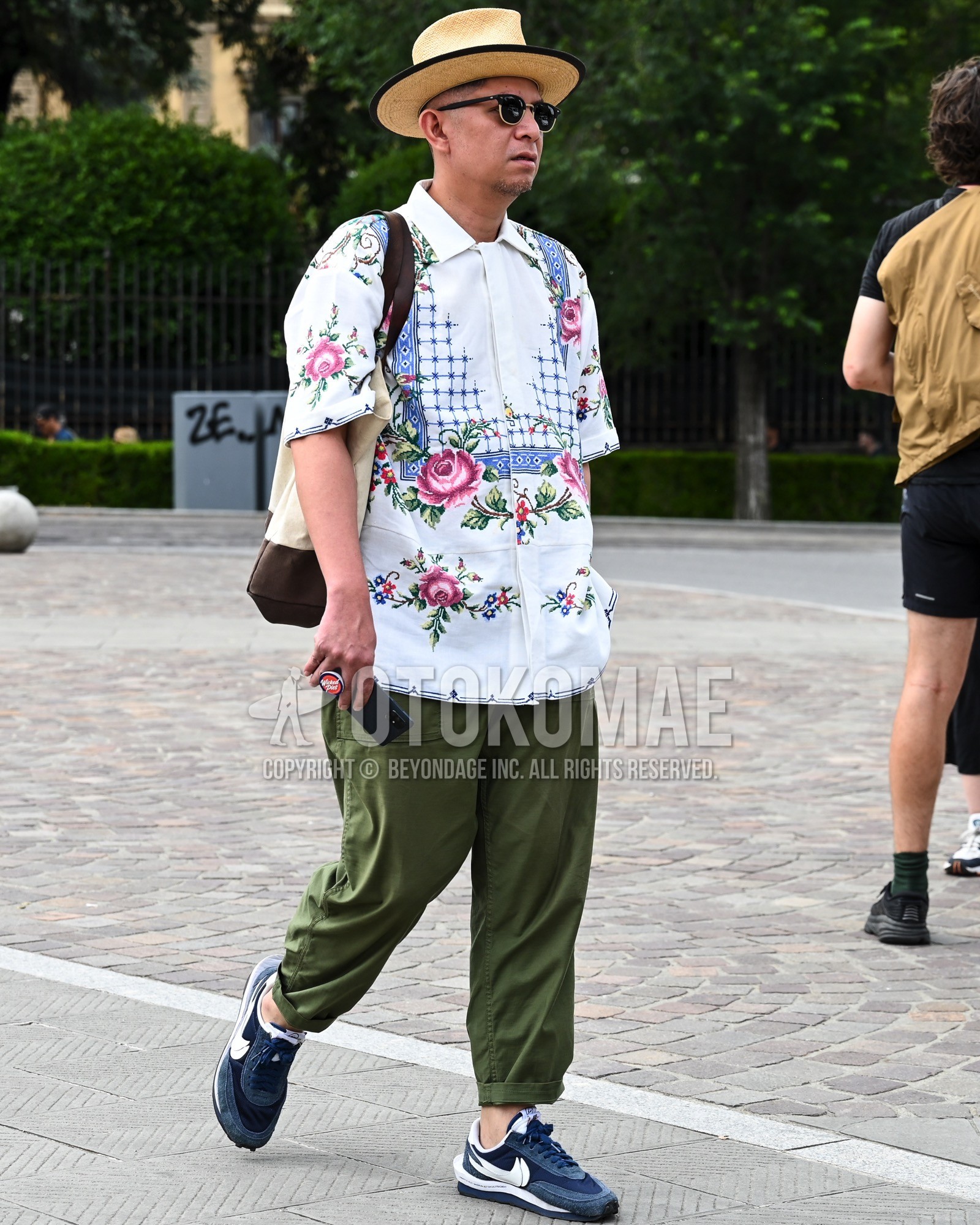 Men's spring summer outfit with beige plain hat, black plain sunglasses, white whole pattern shirt, olive green plain chinos, navy low-cut sneakers, white plain tote bag.