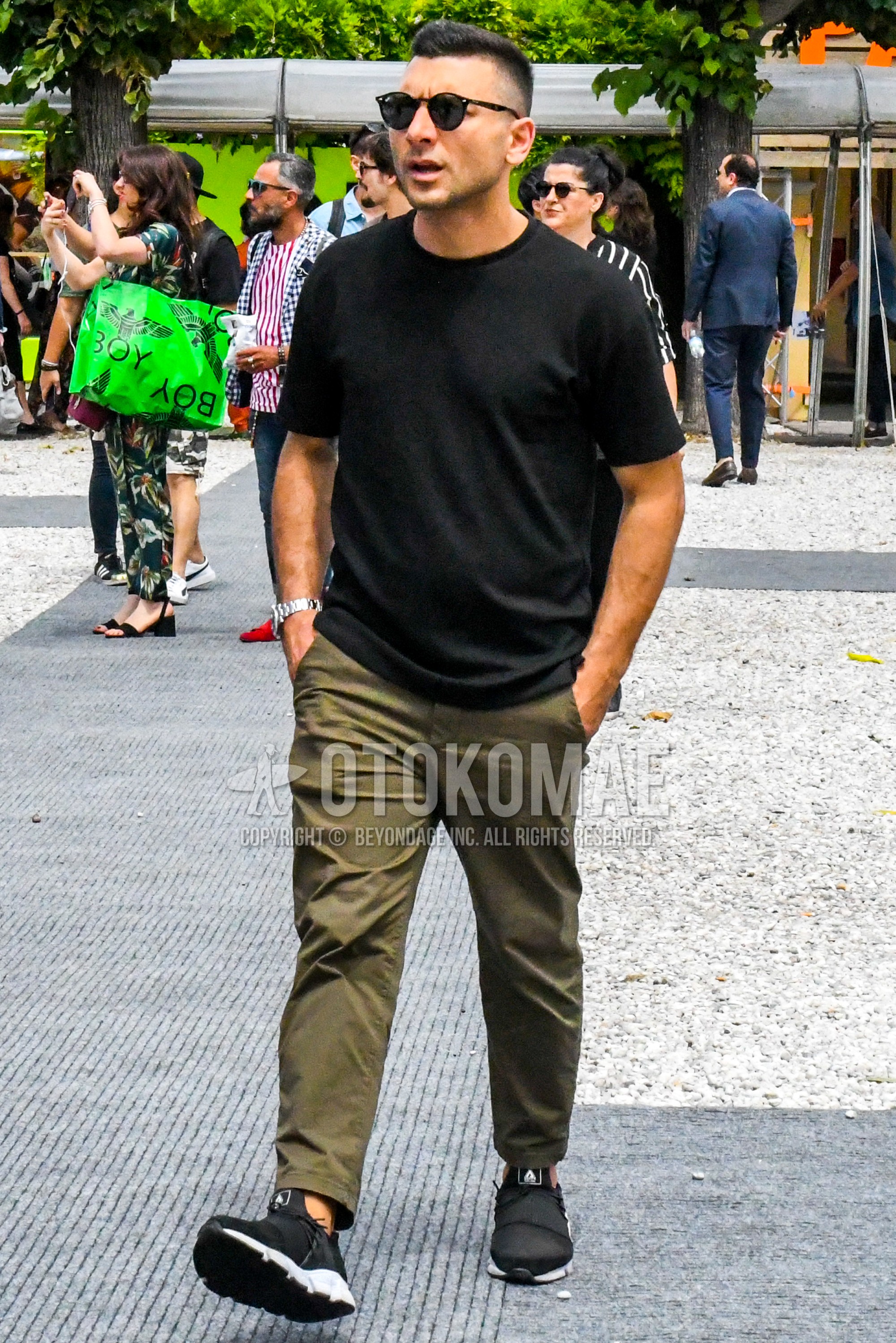 Men's summer outfit with plain sunglasses, black plain t-shirt, green plain ankle pants, black low-cut sneakers.