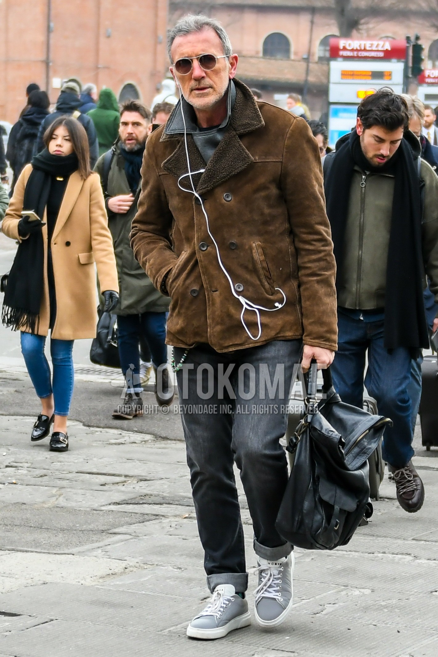 Men's autumn winter outfit with plain sunglasses, brown plain leather jacket, black plain riders jacket, gray plain denim/jeans, gray low-cut sneakers, black plain briefcase/handbag.