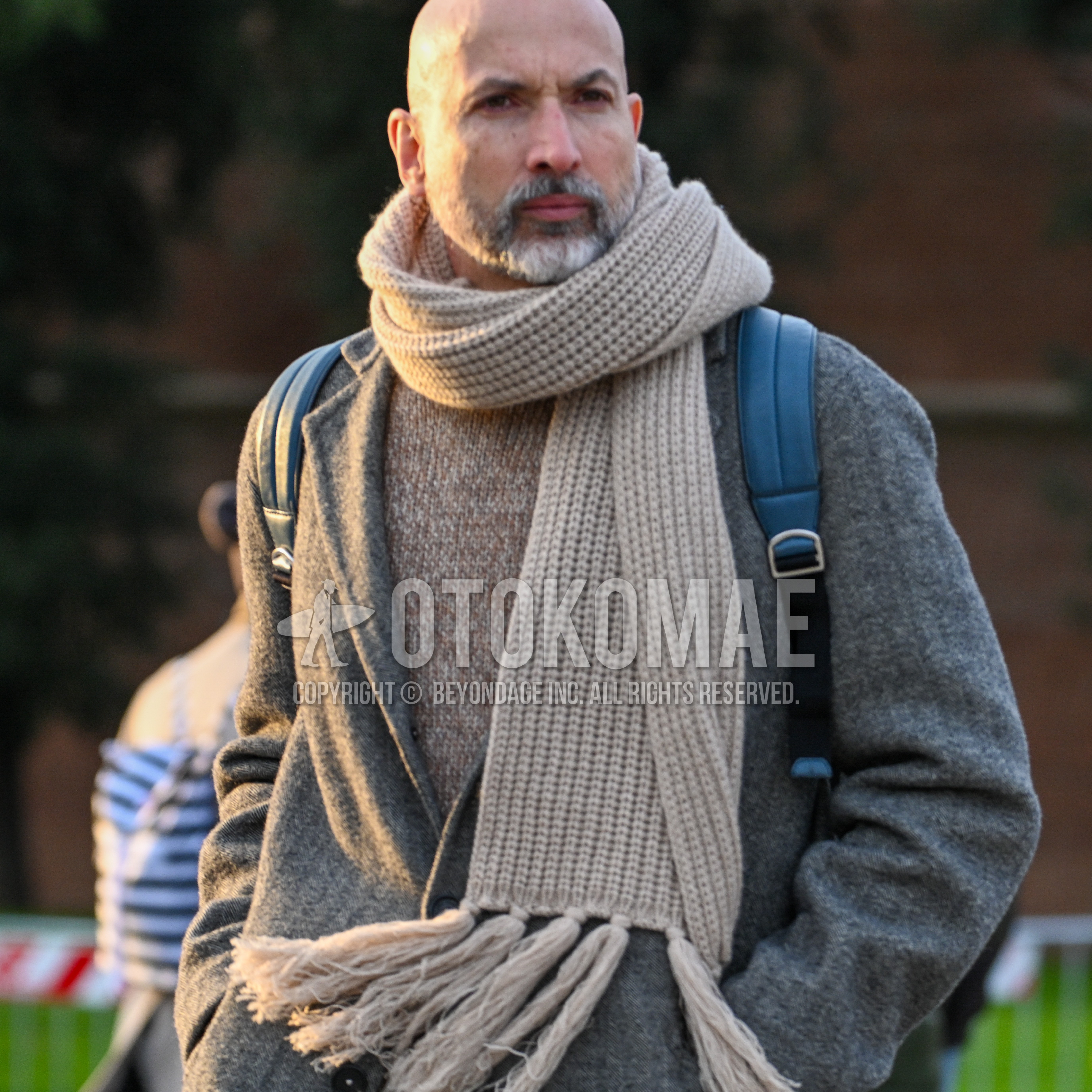Men's autumn winter outfit with beige plain scarf, gray plain chester coat, beige plain sweater, black plain backpack.