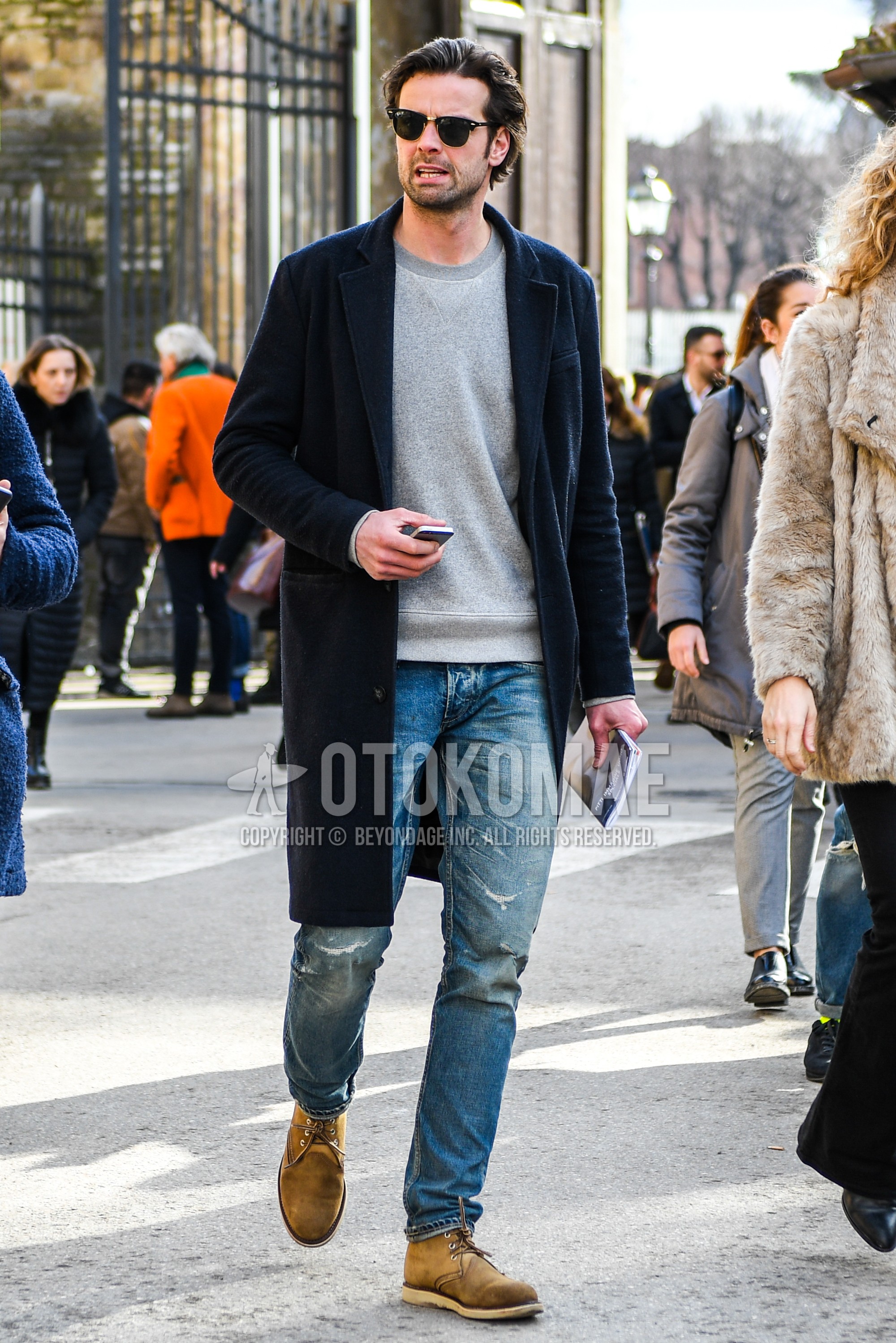 Men's autumn winter outfit with plain sunglasses, black plain chester coat, gray plain sweatshirt, blue plain denim/jeans, beige  boots.