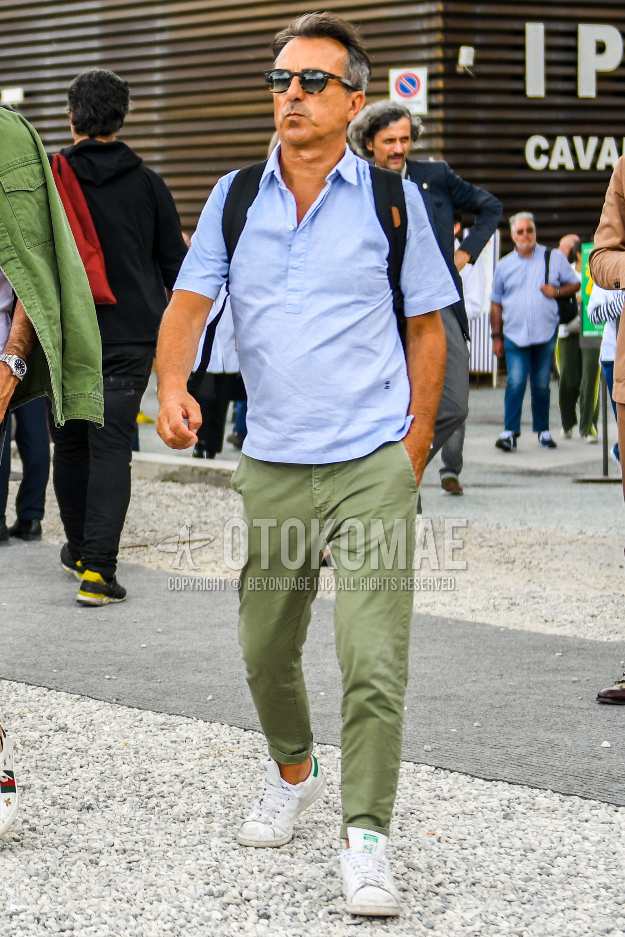 Men's summer outfit with tortoiseshell sunglasses, light blue plain polo shirt, olive green plain chinos, white low-cut sneakers.