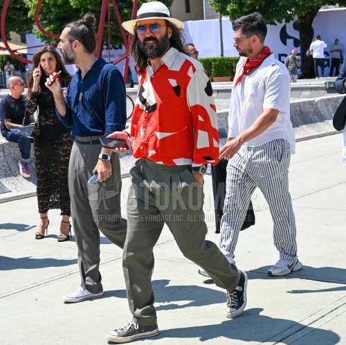 麦わらの白無地のハット、オレンジ無地のサングラス、レッド・白グラフィックのシャツ、グレー無地のスラックス、グレー無地のプリーツパンツ、グレー無地のベルトレスパンツ、黒ローカットのスニーカーを合わせた夏春のメンズコーデ・着こなし。