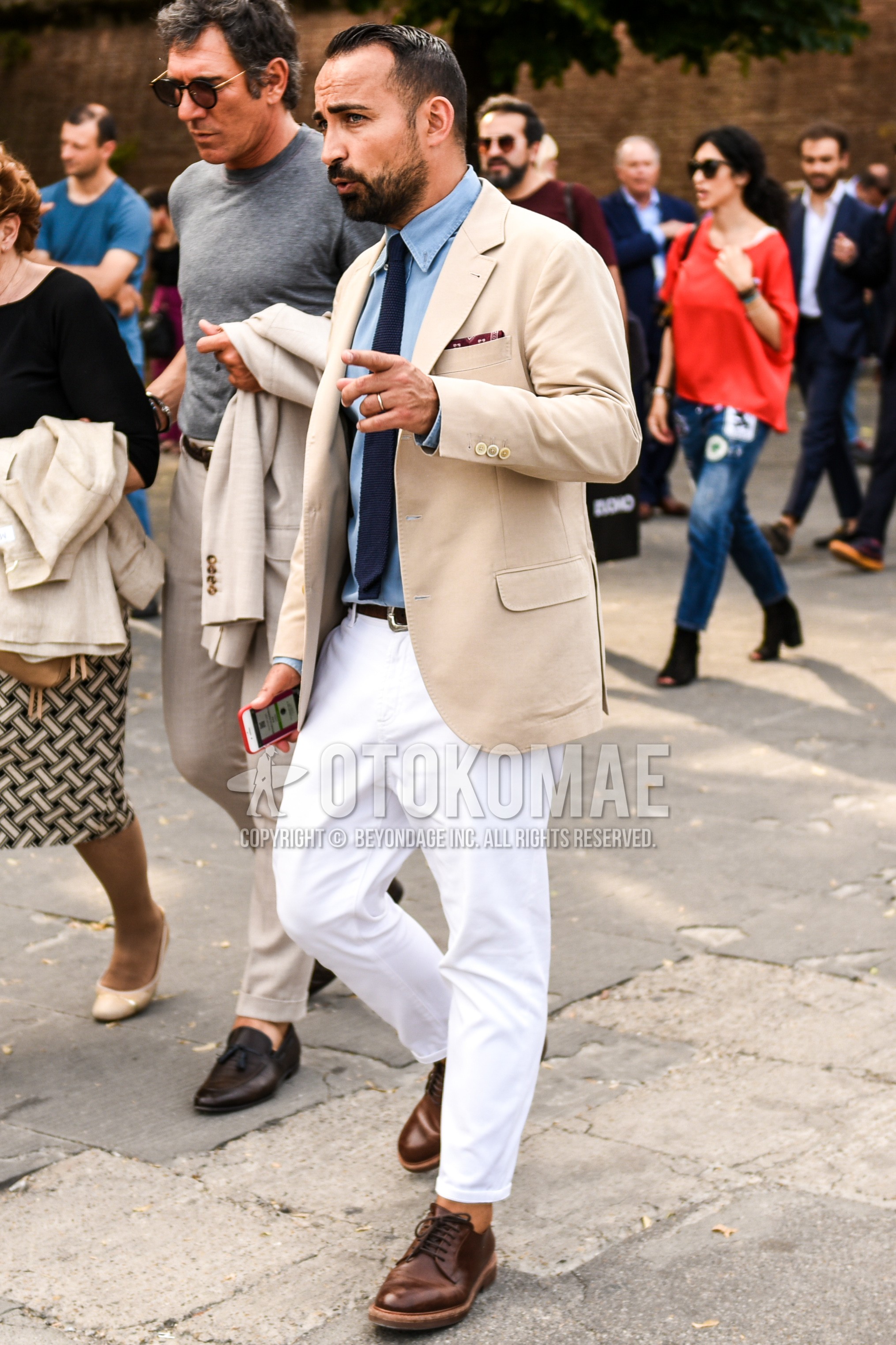 Men's spring autumn outfit with beige plain tailored jacket, light blue plain shirt, white plain cotton pants, brown plain toe leather shoes, navy plain knit tie.