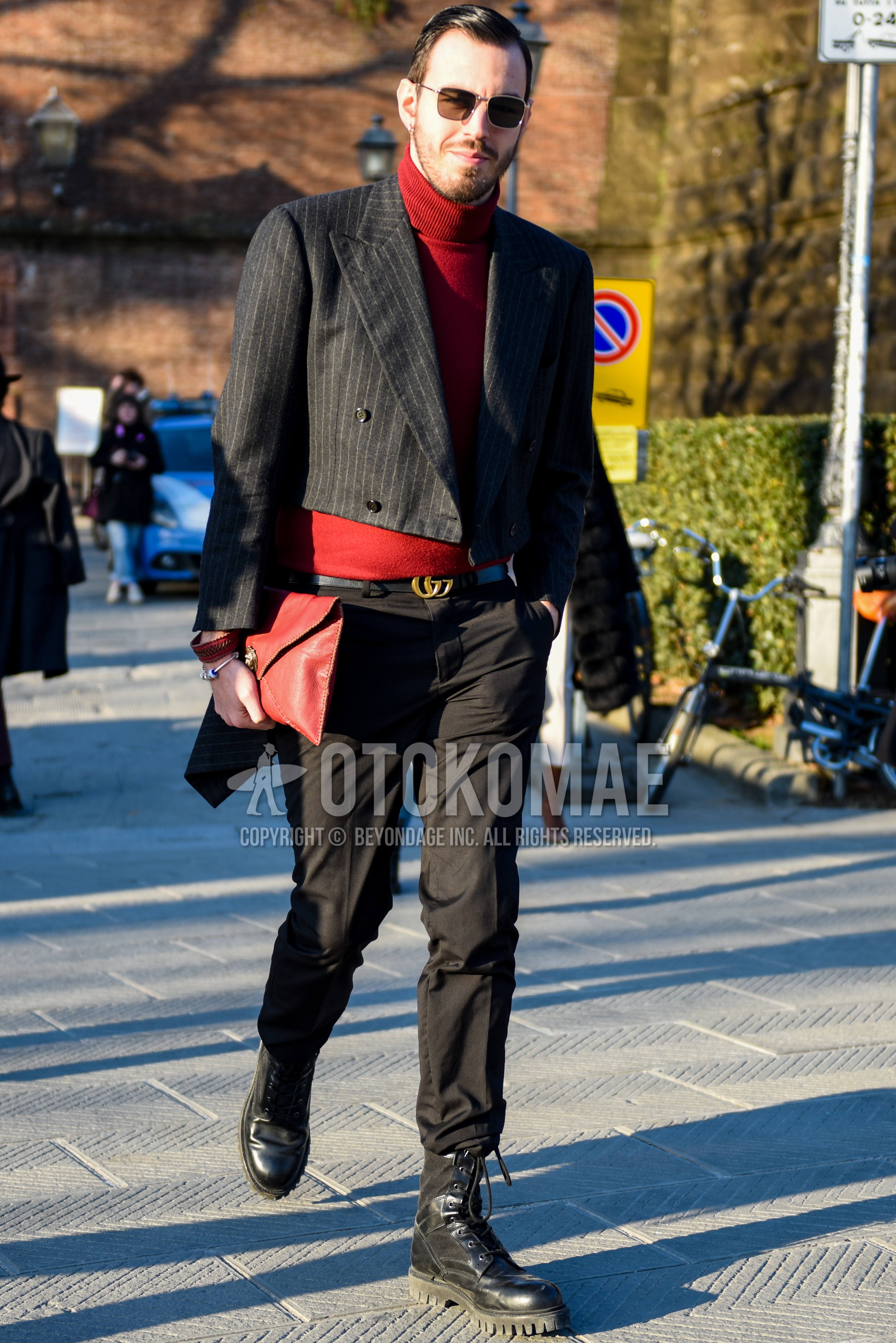 Men's autumn winter outfit with silver plain sunglasses, dark gray stripes tailored jacket, red plain turtleneck knit, black one point leather belt, black plain slacks, black work boots, red plain clutch bag/second bag/drawstring bag.