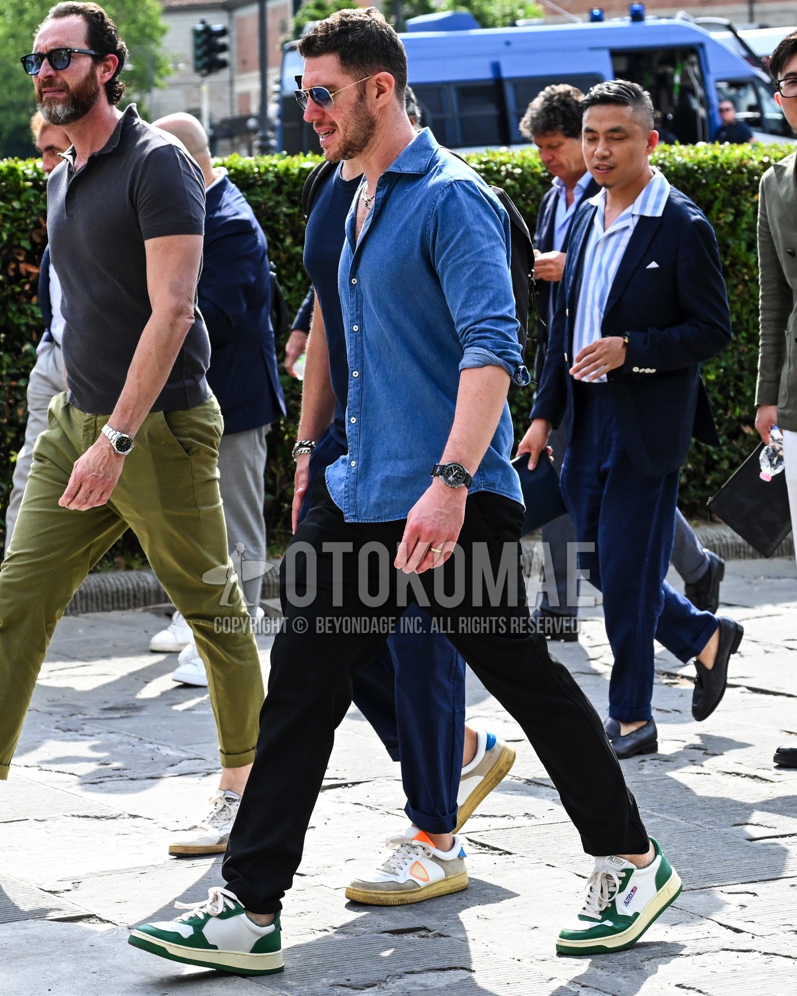 Men's spring summer autumn outfit with blue plain sunglasses, blue plain denim shirt/chambray shirt, black plain chinos, white green low-cut sneakers.
