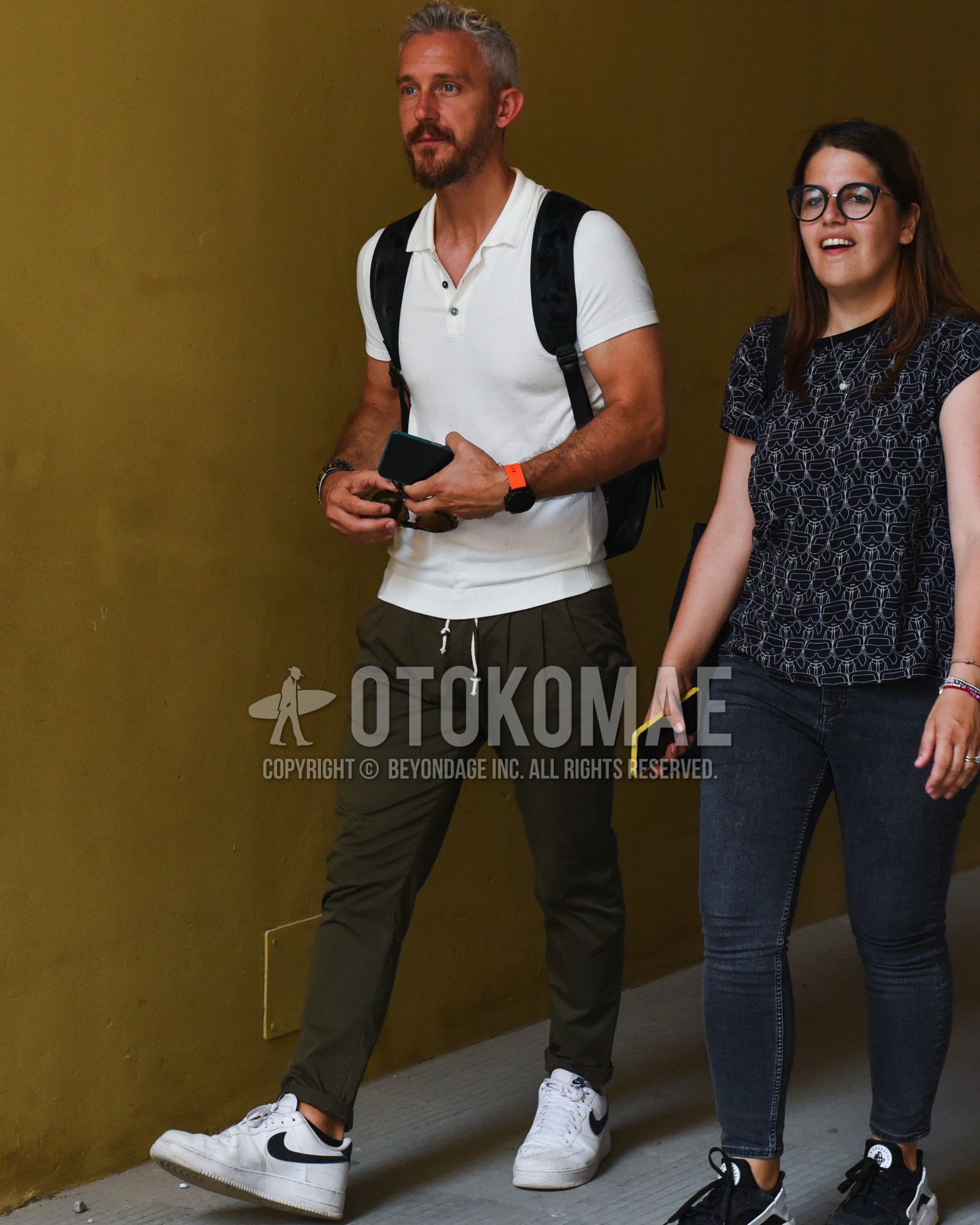 Men's spring summer outfit with white plain polo shirt, olive green plain easy pants, white low-cut sneakers, black plain backpack.