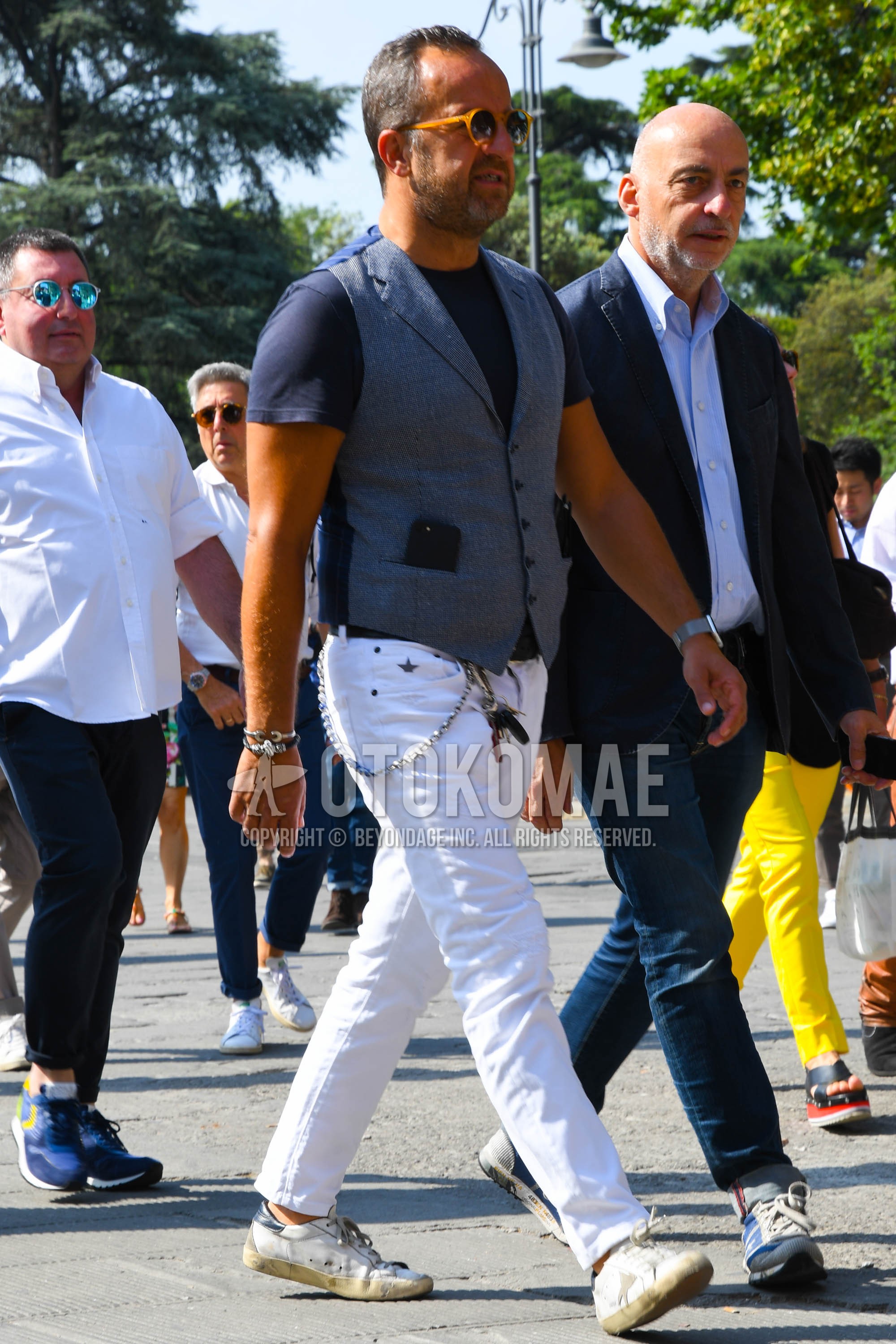Men's spring summer outfit with beige plain sunglasses, gray plain gilet, navy plain t-shirt, white plain denim/jeans, white low-cut sneakers.
