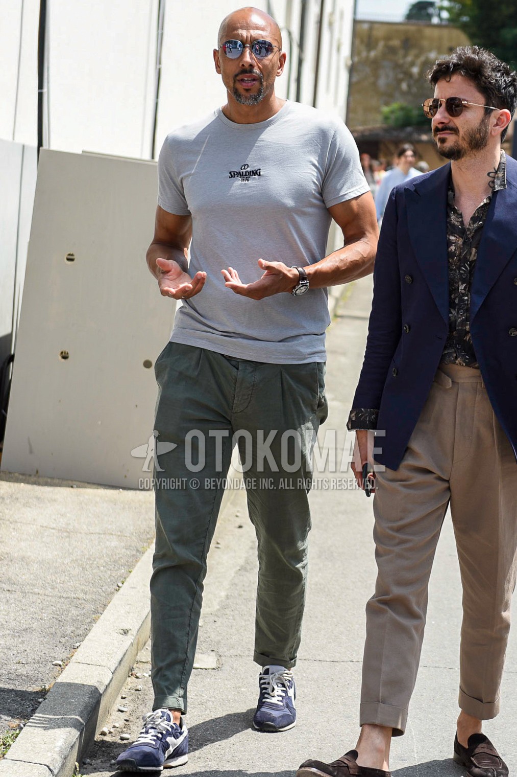 Men's summer outfit with silver plain sunglasses, beige plain t-shirt, olive green plain cotton pants, blue low-cut sneakers.