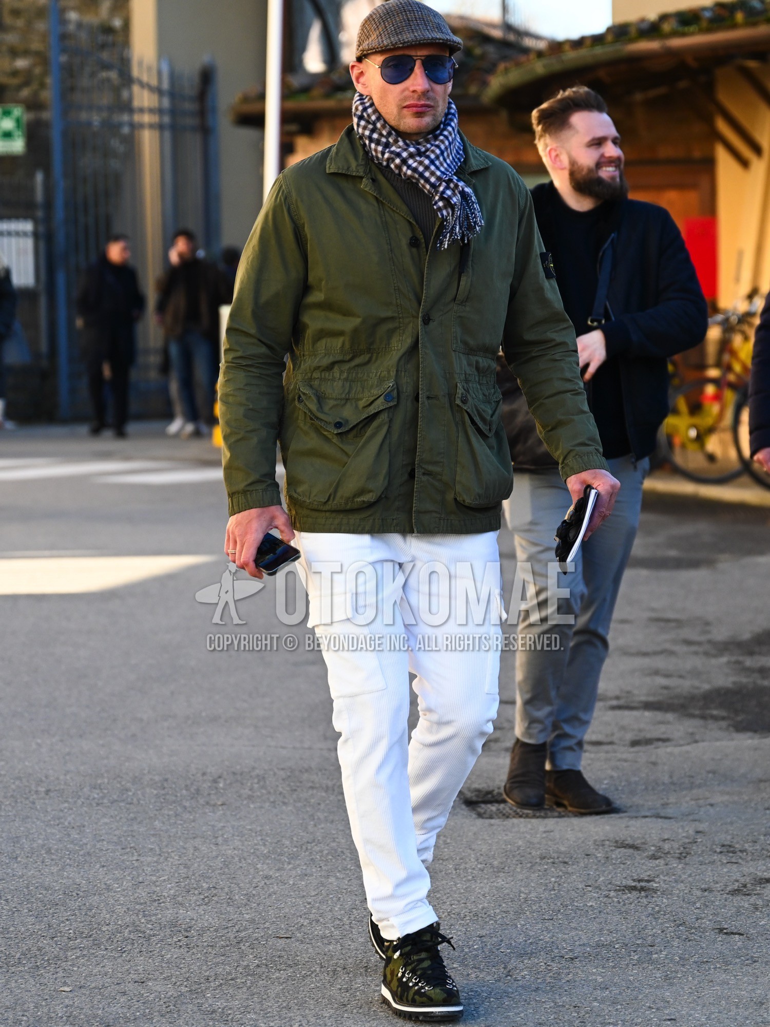 Men's autumn winter outfit with gray check hunting cap, white blue brown check scarf, olive green plain military jacket, olive green plain sweater, white plain cargo pants, olive green low-cut sneakers.