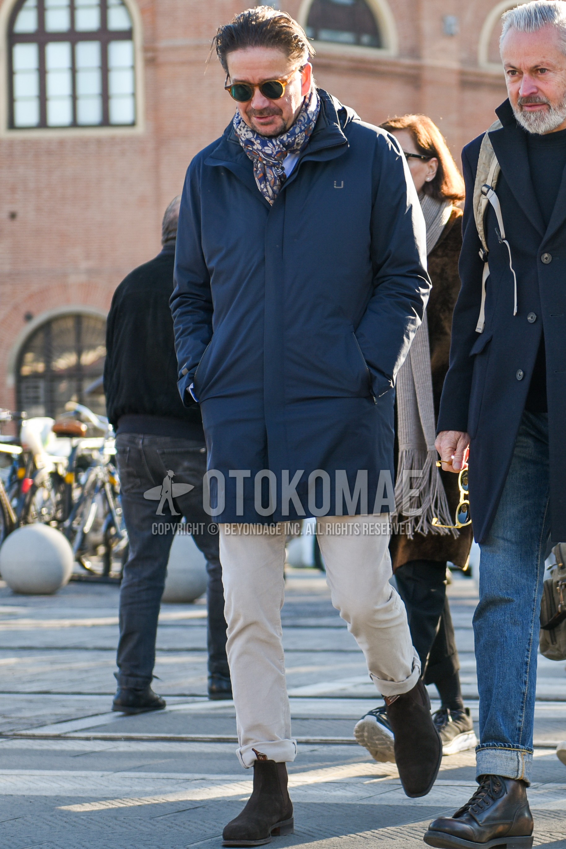 Men's autumn winter outfit with brown plain sunglasses, multi-color scarf scarf, dark gray plain hooded coat, beige plain chinos, brown side-gore boots.
