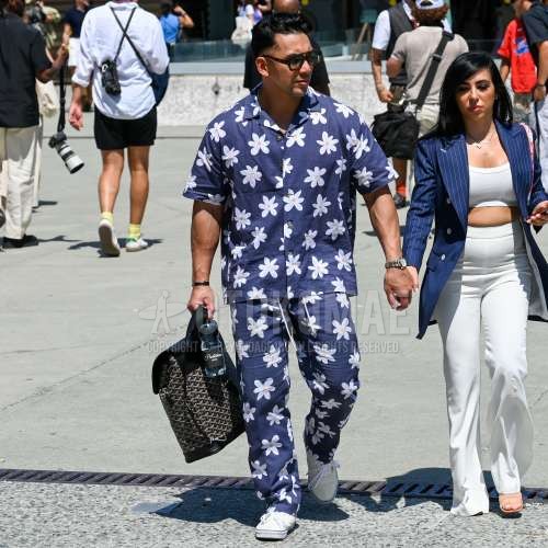 ブラウンべっ甲のサングラス、開襟　オープンカラーのネイビー総柄のシャツ、ネイビー総柄のイージーパンツ、白ローカットのスニーカー、マルチカラーバッグのバックパック、ネイビー総柄のカジュアルセットアップを合わせた夏春のメンズコーデ・着こなし。