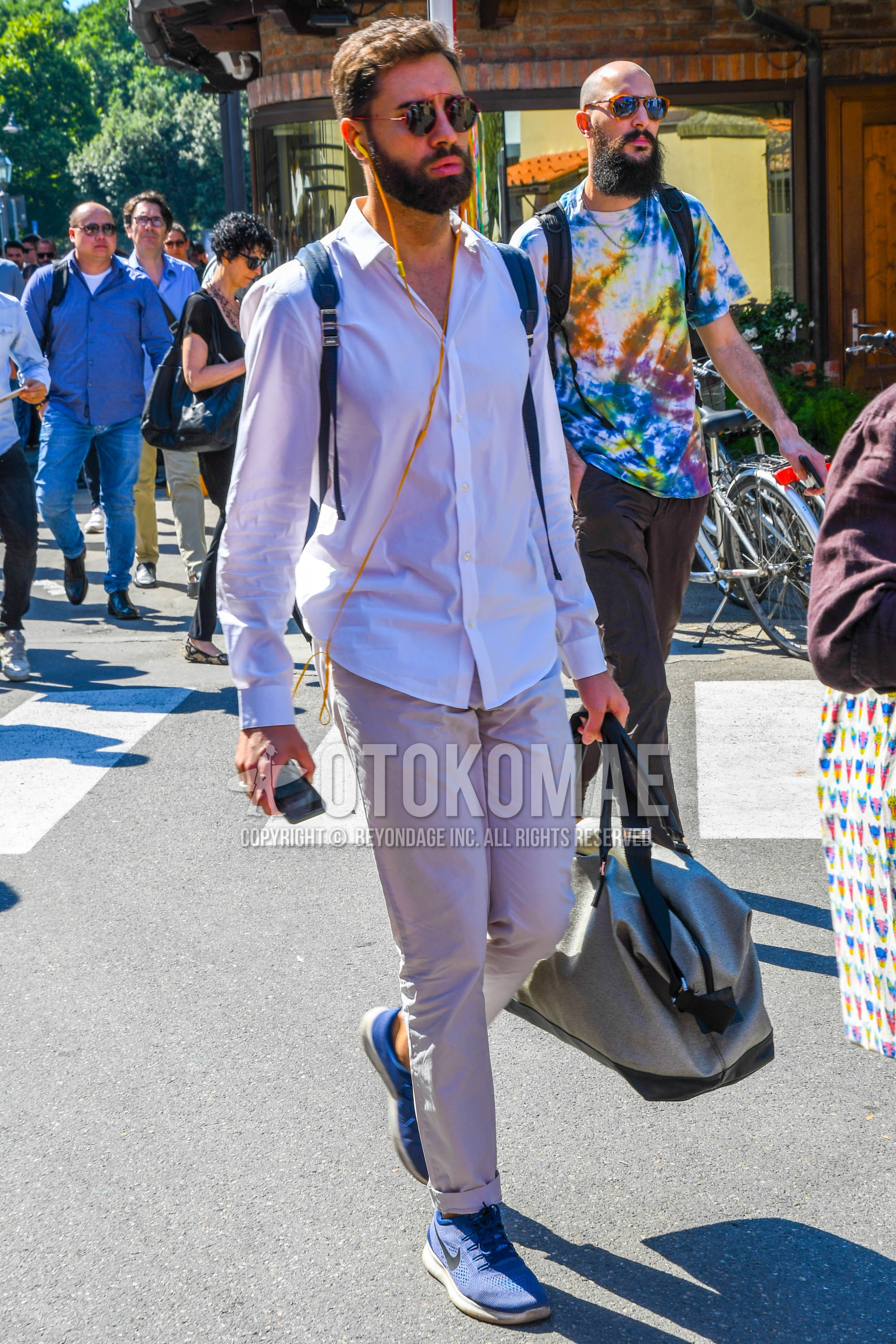 Men's spring summer outfit with plain sunglasses, white plain shirt, beige plain chinos, blue low-cut sneakers.