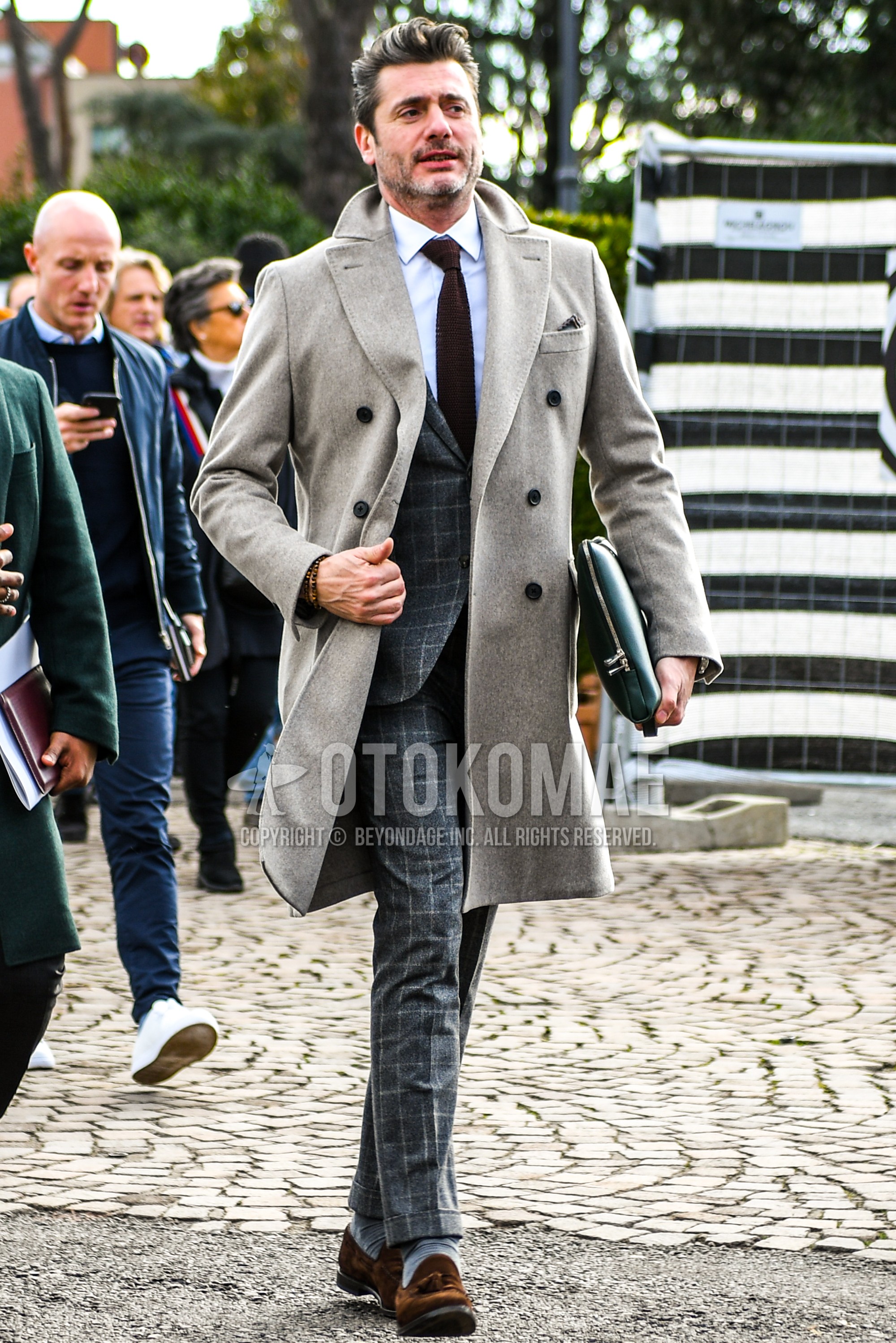 Men's autumn winter outfit with beige plain chester coat, white plain shirt, black plain clutch bag/second bag/drawstring bag, gray check suit, brown plain necktie.