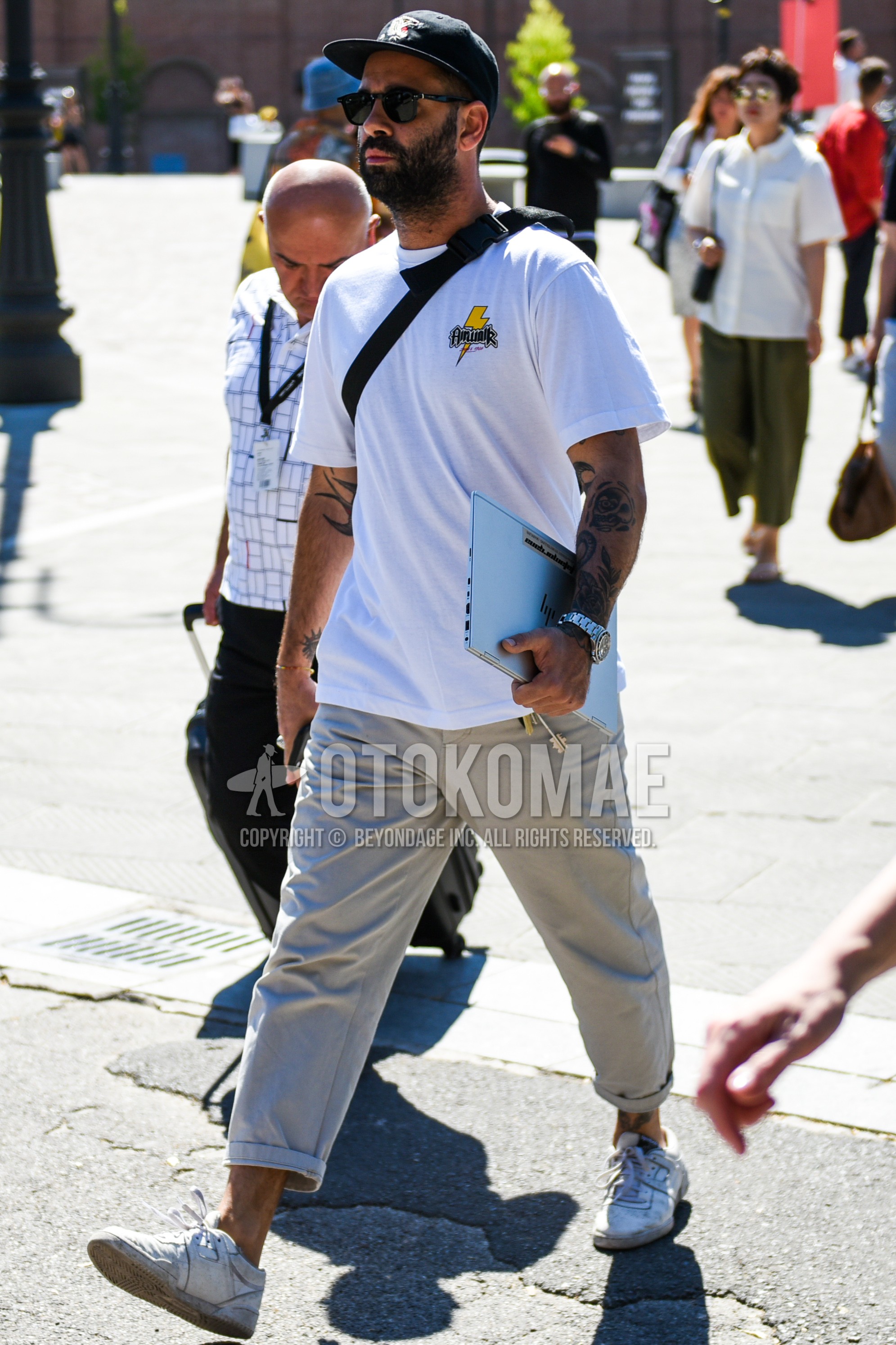 Men's summer outfit with black graphic baseball cap, white one point t-shirt, beige plain chinos, white low-cut sneakers.