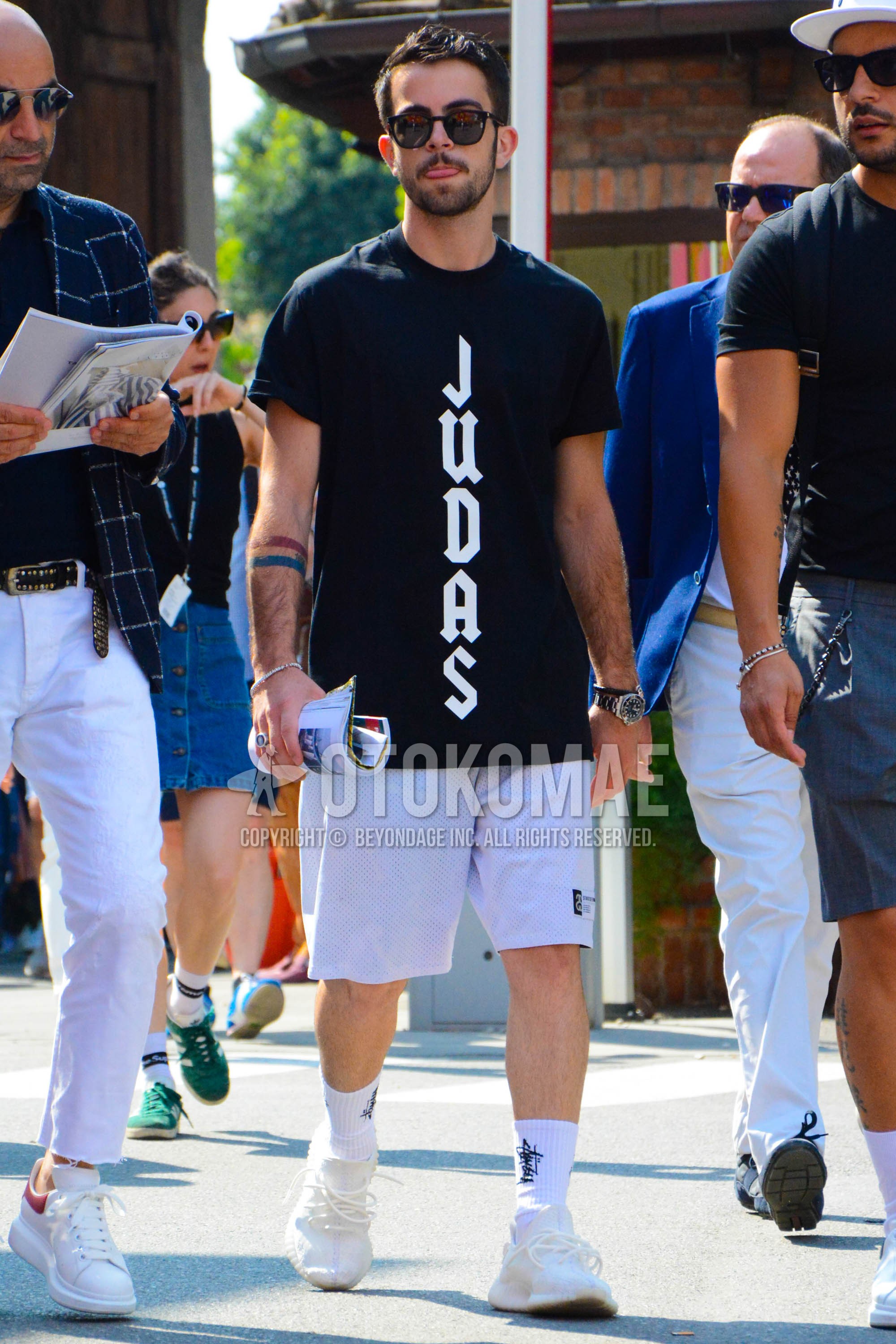 Men's summer outfit with plain sunglasses, black graphic t-shirt, white plain short pants, white graphic socks, white low-cut sneakers.