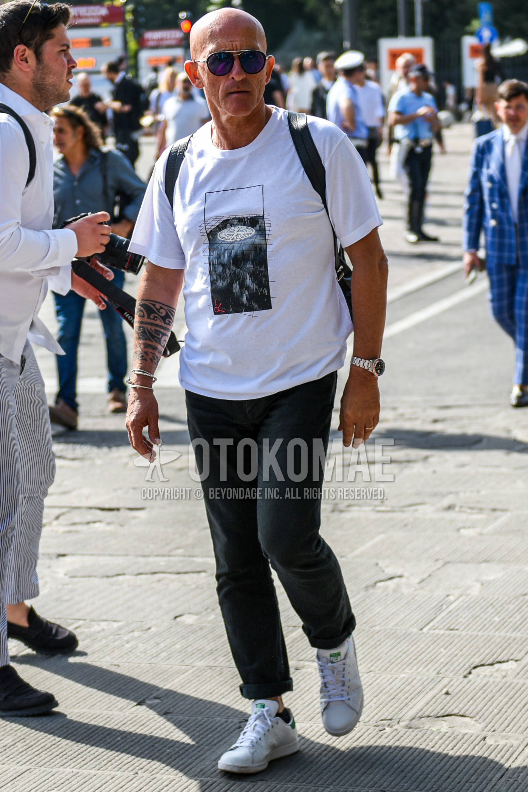 Men's summer outfit with silver plain sunglasses, white graphic t-shirt, dark gray plain cotton pants, white low-cut sneakers.